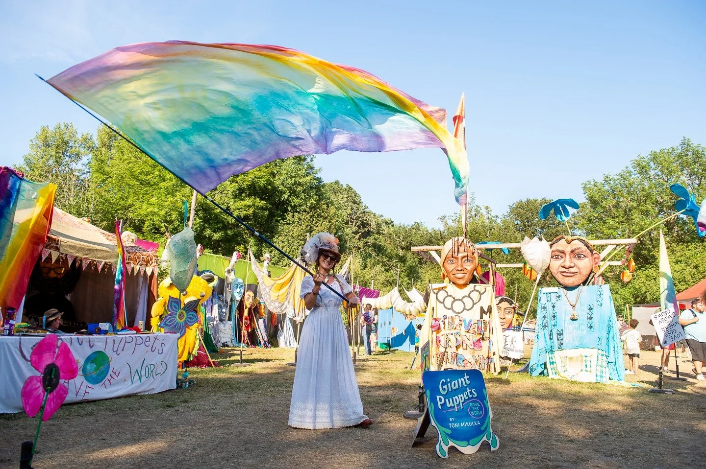 Festival with large, colorful puppets, tents, and decorations outdoors on sunny day.
