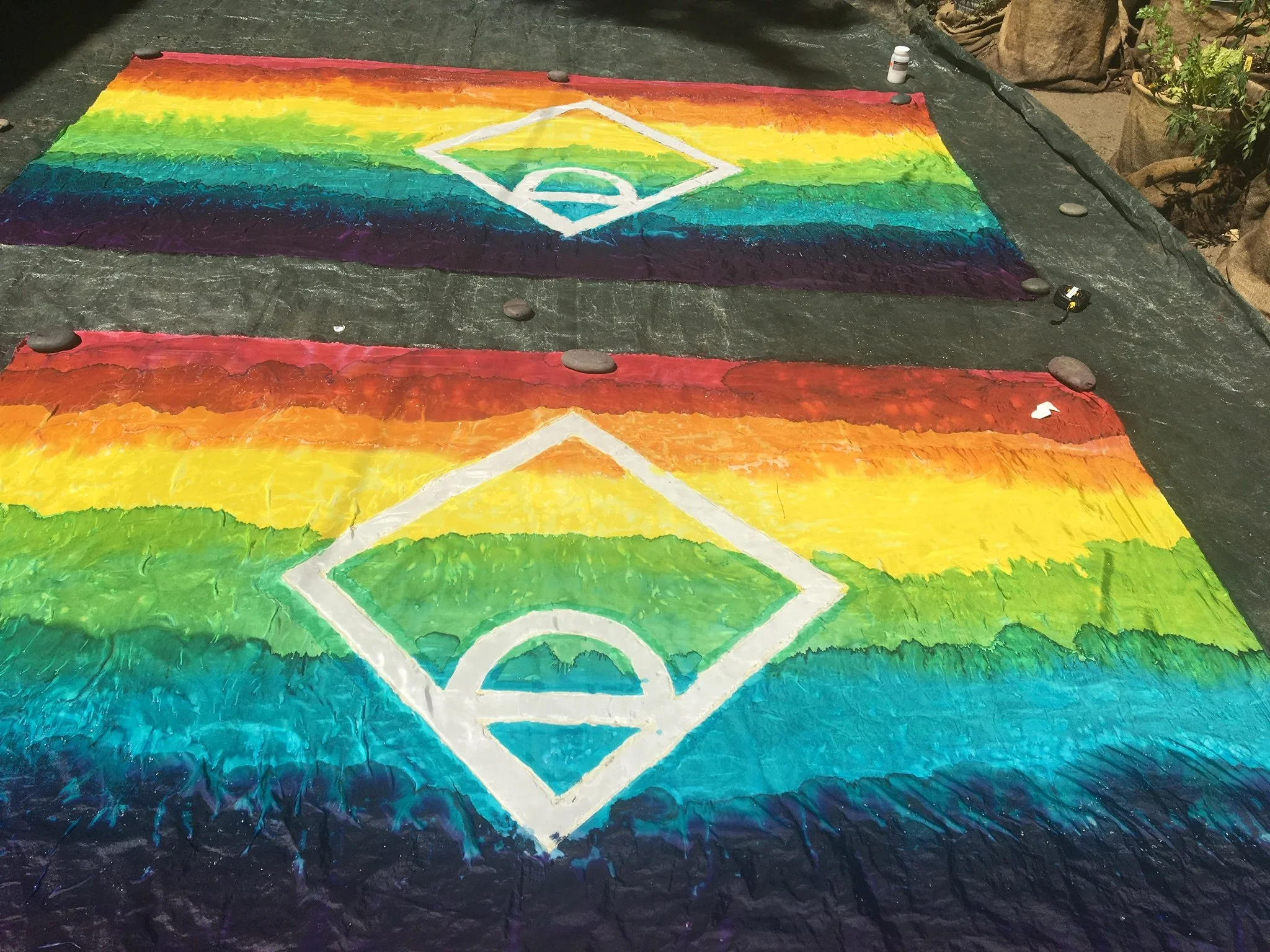 Two large basketball court paintings on the ground, painted with rainbow colors representing the LGBTQ+ pride flag. Each court features a white basketball court outline at the center.