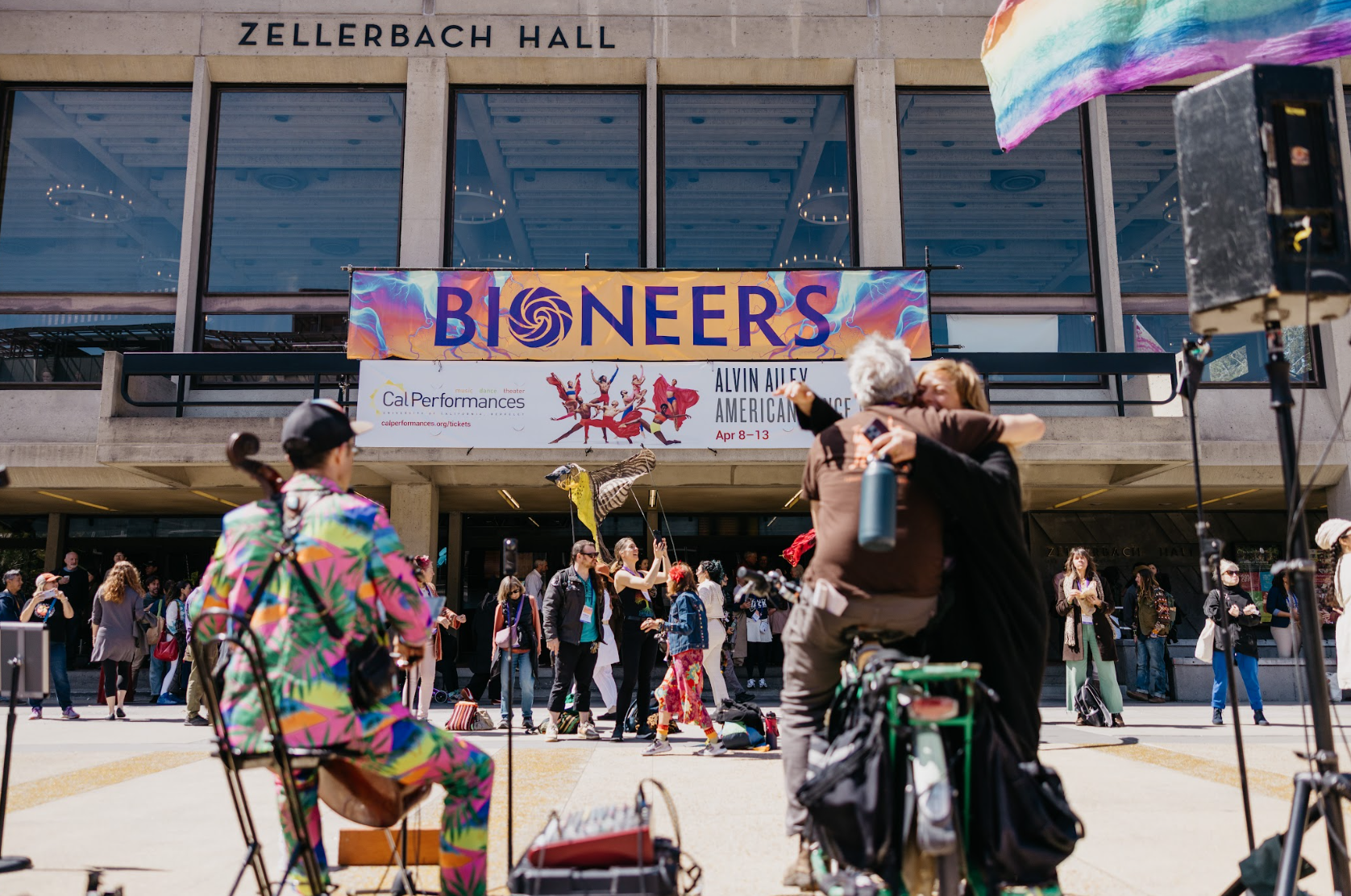 People gathered outside Zellerbach Hall for a performance event, with street performers in colorful costumes and a crowd of onlookers.
