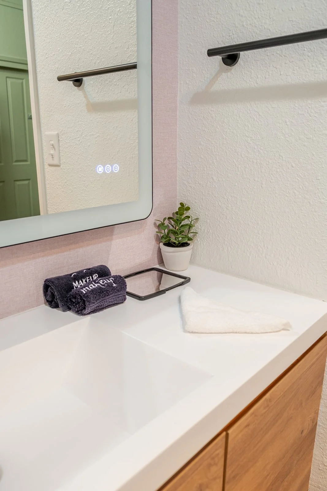Bathroom vanity with a mirror, a small potted plant, folded towel, and a handheld mirror.