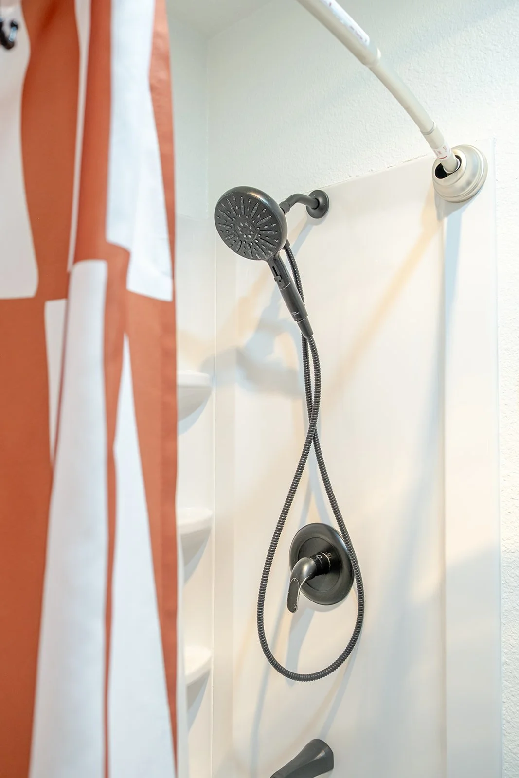 Handheld showerhead and faucet in a shower with a partially visible curtain on the left.