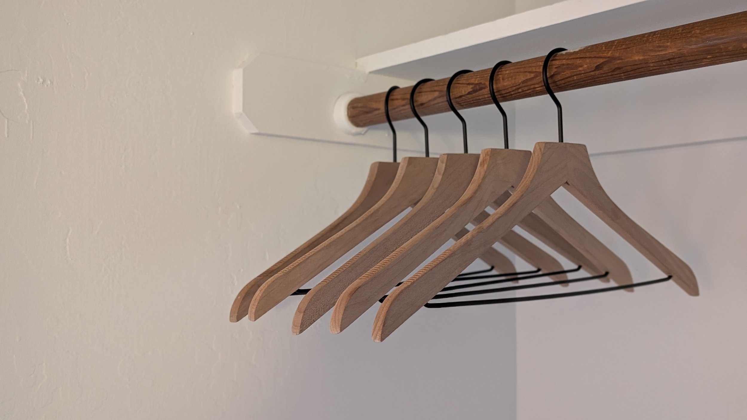 A row of wooden hangers hanging on a wooden rod inside a closet.