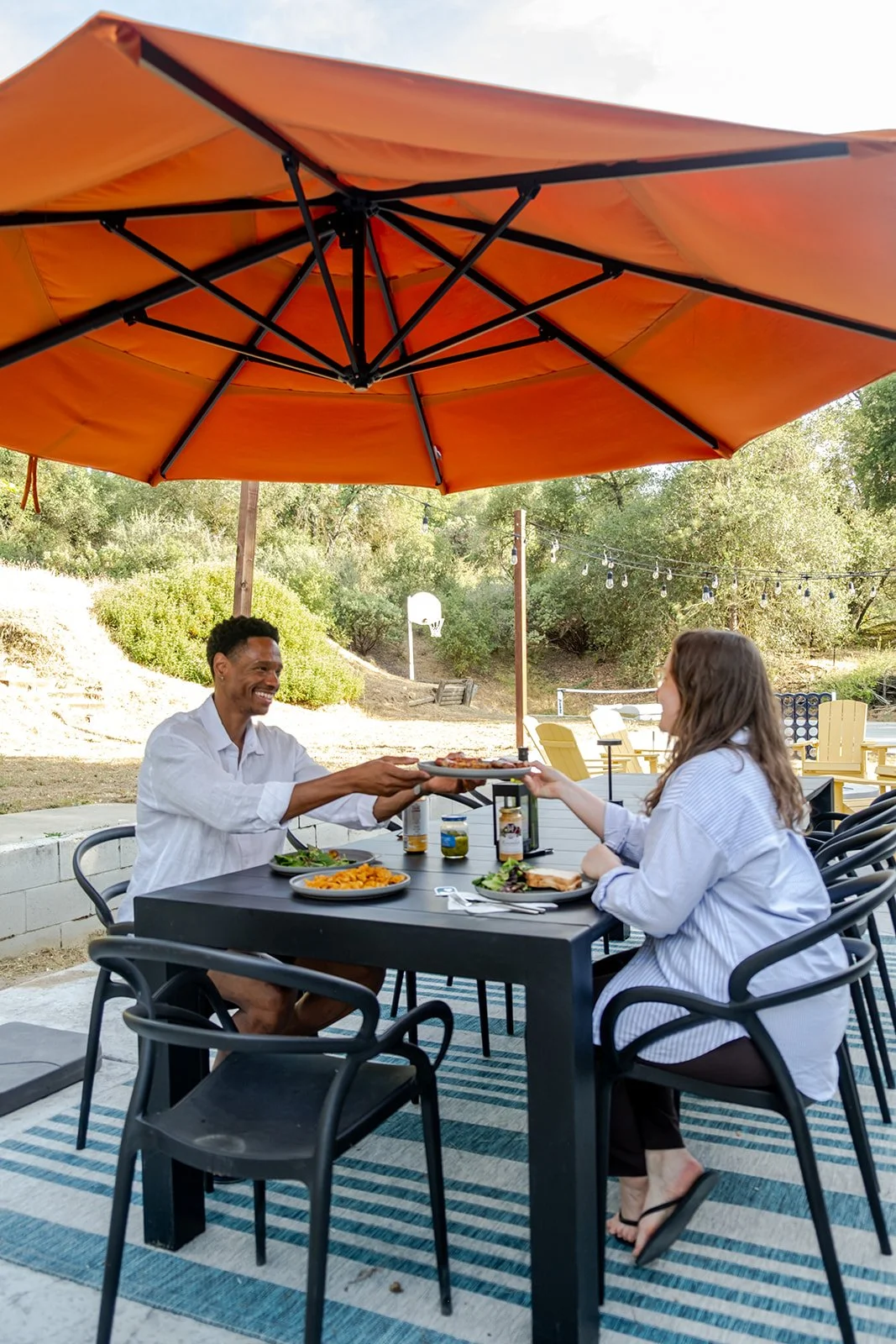 People enjoying a meal outdoors under an orange patio umbrella.