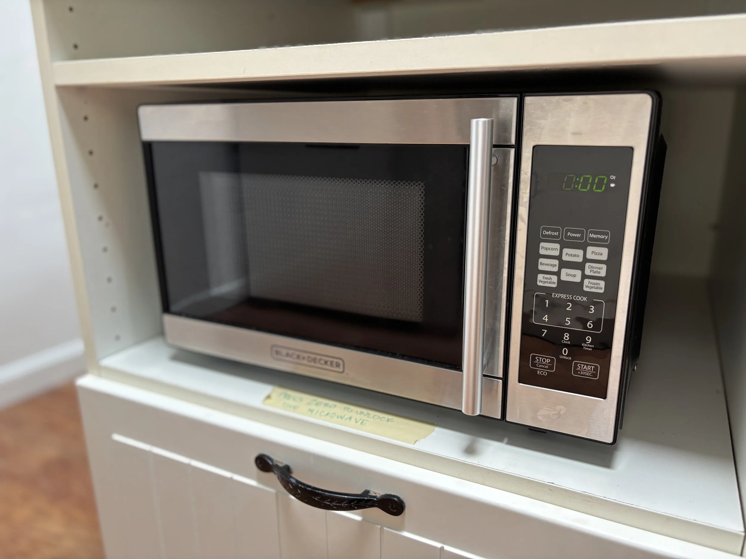 A microwave oven placed inside a white cabinet on a countertop, with a digital display showing 0:00 and various control buttons.
