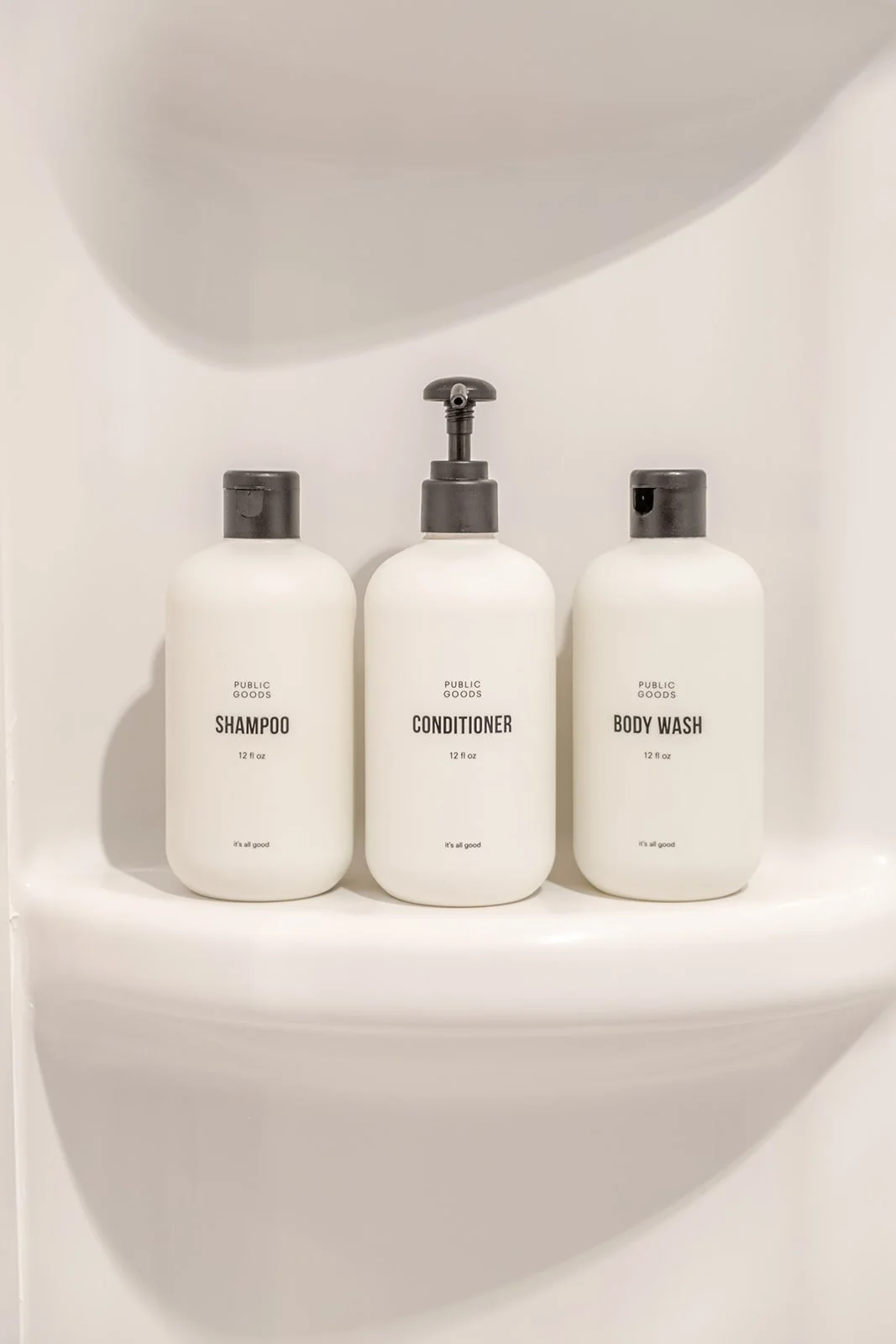 Three white bottles labeled shampoo, conditioner, and body wash on a white shelf under a sink