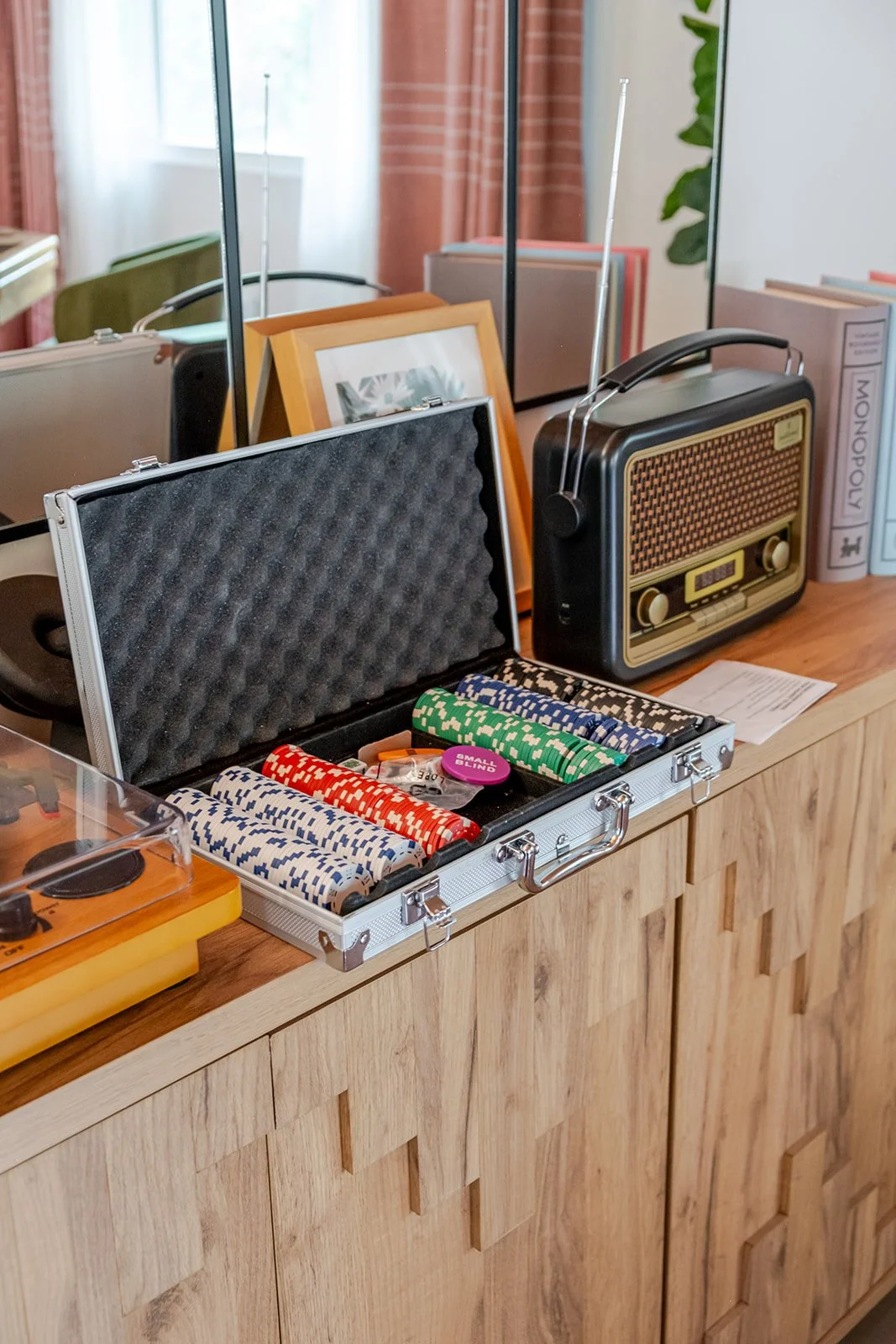 A collection of vintage items on a wooden cabinet, including a turntable, poker chips in a suitcase, a radio, and framed pictures in the background.