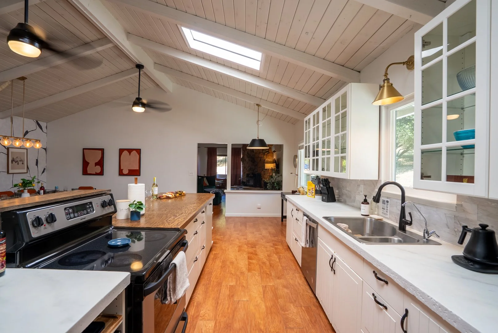 Bright kitchen with white cabinetry, wooden countertops, and skylight, open to living room with fireplace.