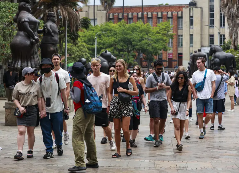Grupo de turistas caminando en ciudad con esculturas de animales y árboles al fondo.