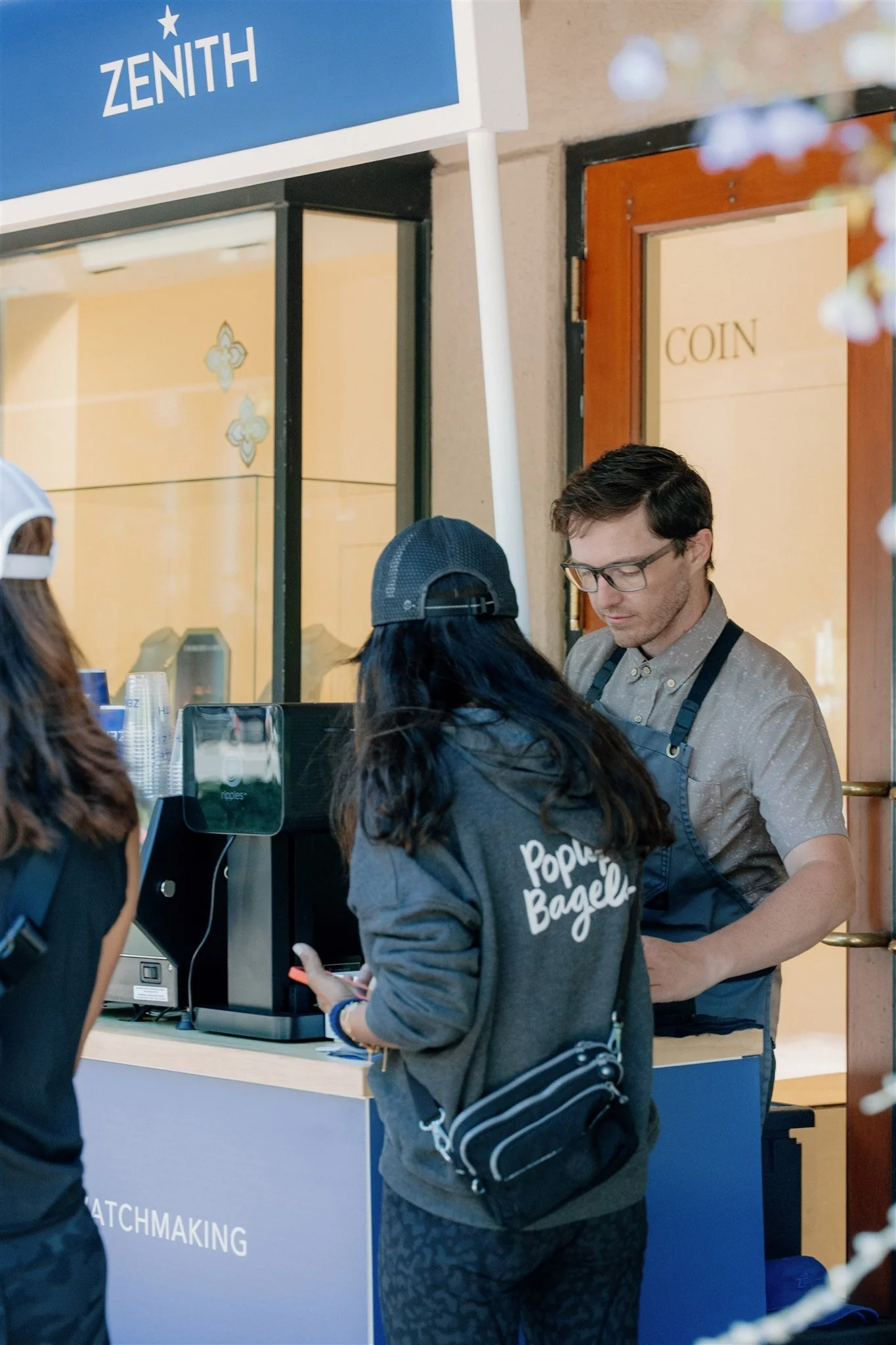 People standing at an activation coffee cart catering counter outside a store with a sign that reads 'ZENITH' with a private barista pouring espresso drinks and latte art