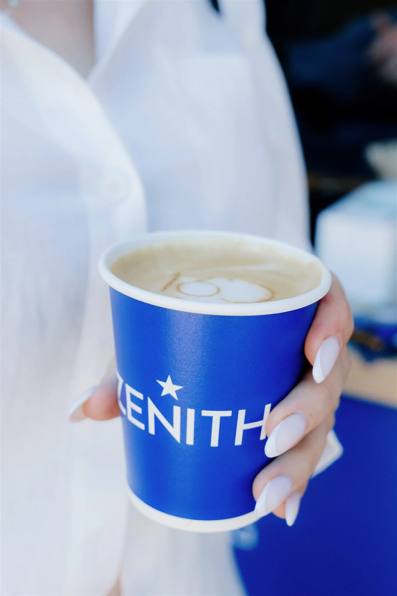 Person holding a blue cup of coffee with the word 'ZENITH' on it, close-up shot.