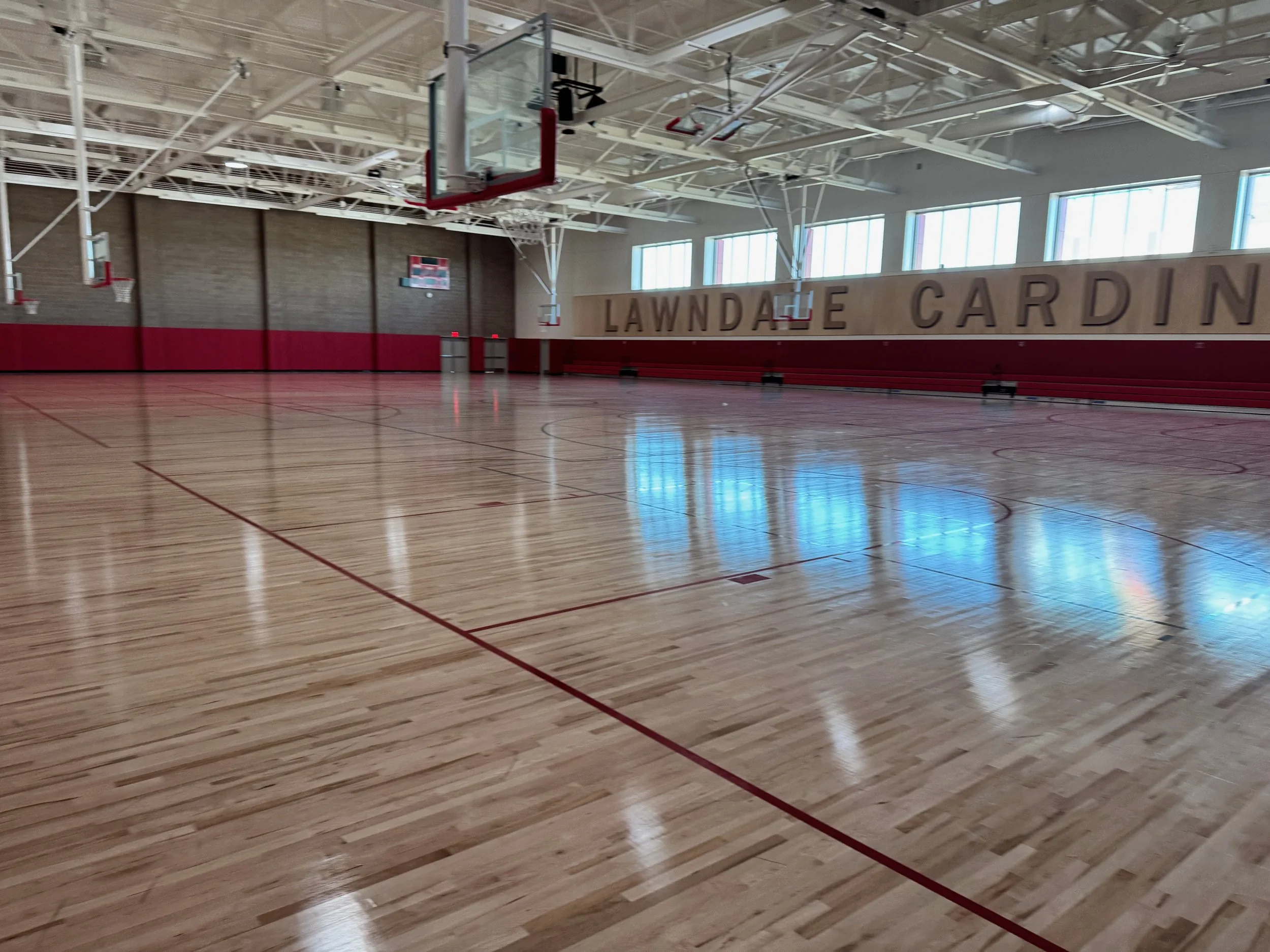 Indoor basketball gymnasium with wooden floor and multiple basketball hoops, featuring red and white detailing.