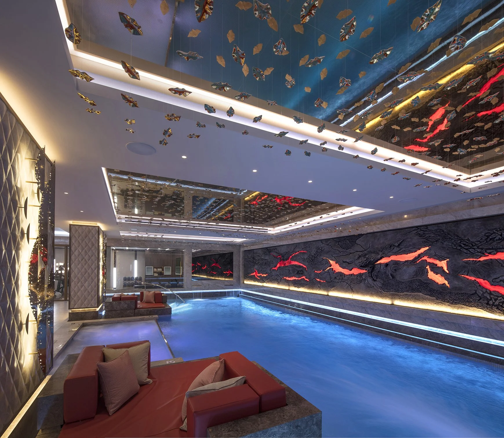 Indoor swimming pool area with modern decor, colorful abstract wall art with glowing red and orange accents, and suspended decorative fish-shaped ornaments from the ceiling.
