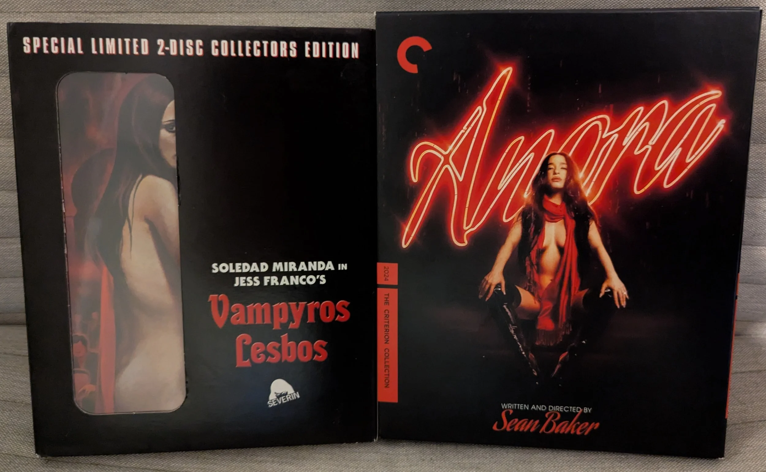 Two movie cases. Left is "Vampyros Lesbos". Black cover with title. Back half of a woman's naked body visibile through a cutout in the slipcase. On the right is "Anora". Title in neon. A woman in skimpy red clothes with legs open looking at camera.