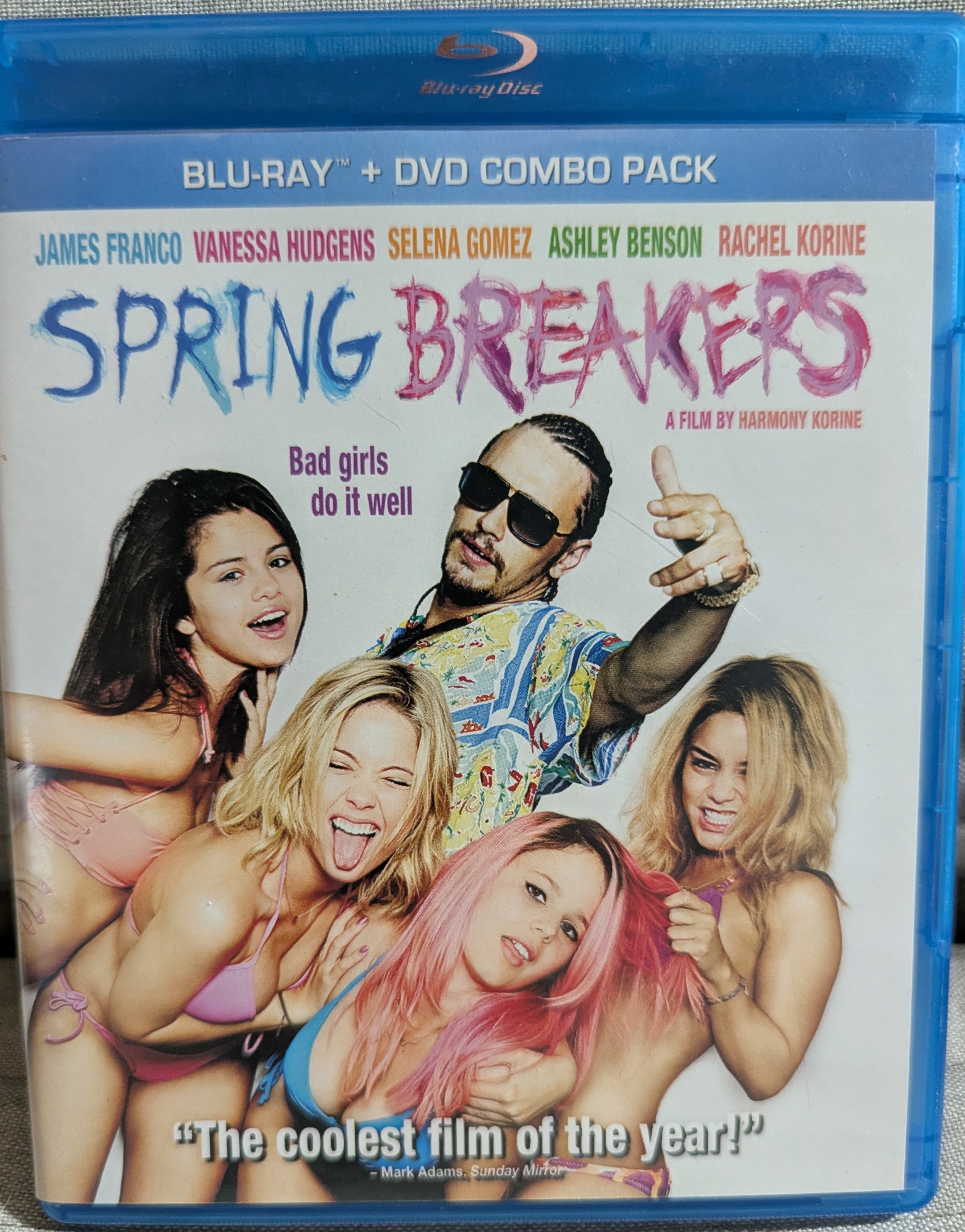 Blu-ray case for "Spring Breakers". Movie title and name of cast at top. Four women wearing bikinis huddled together are below, surrounded by James Franco in character as "Alien" with cornrow hairstyle, hand pointed like a gun. All white background.