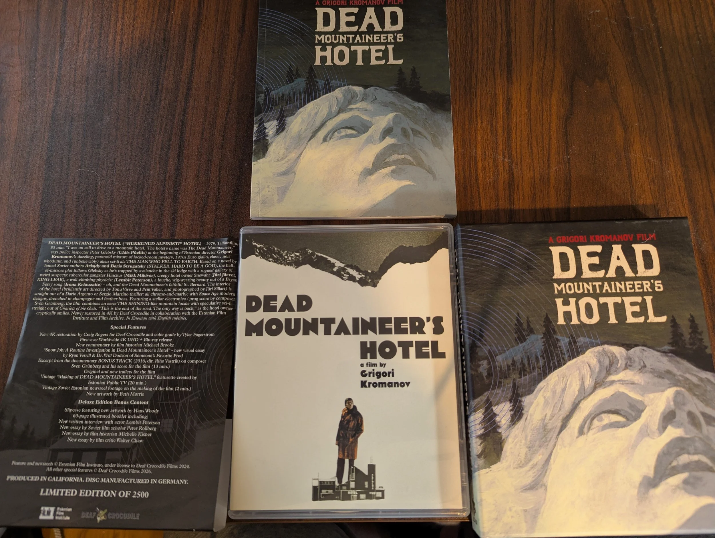 The Blu-ray case, booklet, hard box case, and J-card sheet laid out on a wooden desk with the booklet on top of the other three in a row.  Booklet and hard box have same image.