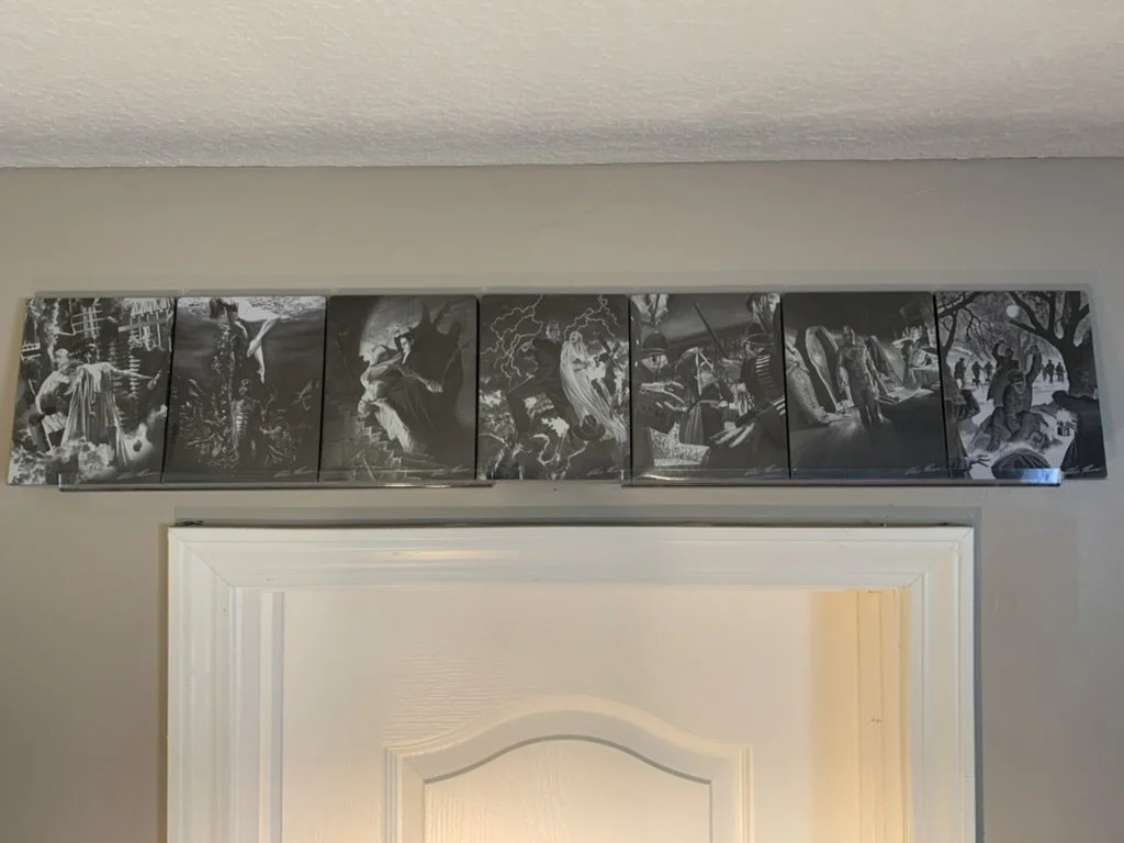 A row of steelbook Blu-ray cases sit vertically aligned on a shelf over a doorframe and beige wall. They all have black and white images of the monsters featured in their movie in a familiar setting, like the Wolf Man in a forest.