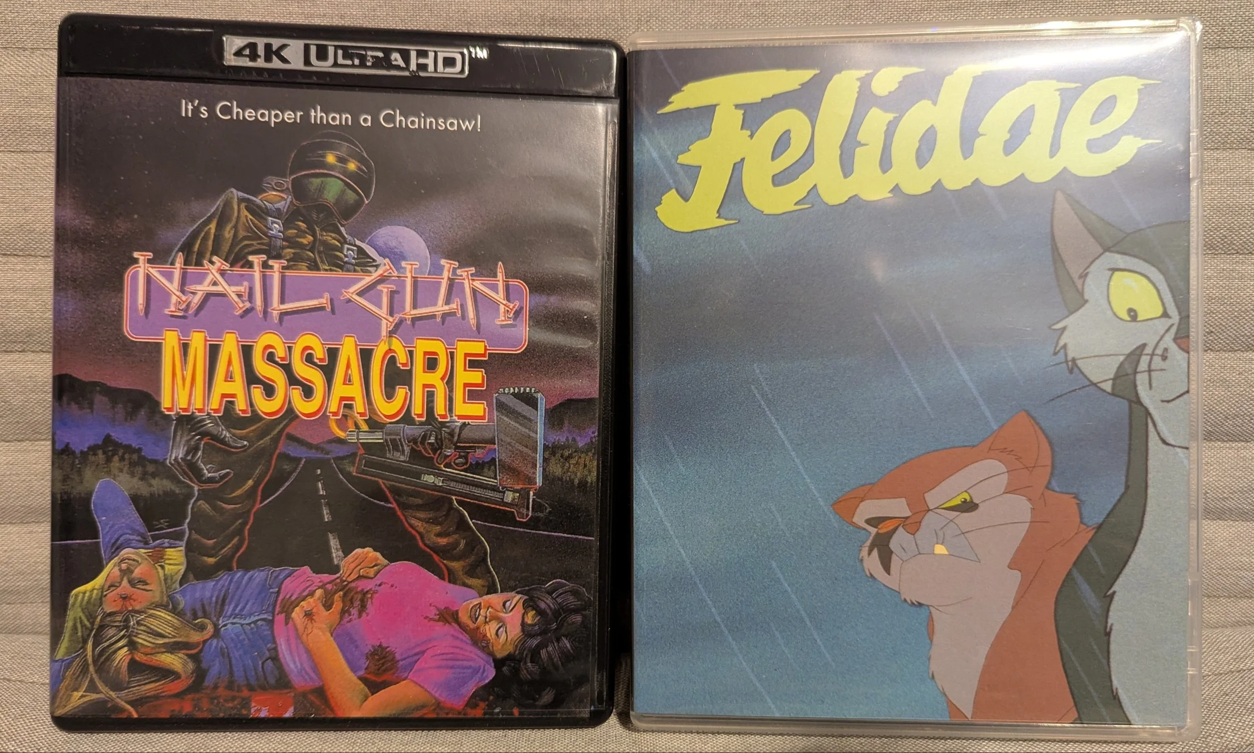 Two movie cases. Nail Gun Massacre case on left. Night scene, two dead woman lie on a highway bleeding with a man in all black standing over them with a nailgun. On right is Felidae. Two animated cats outside under clouds and rain.