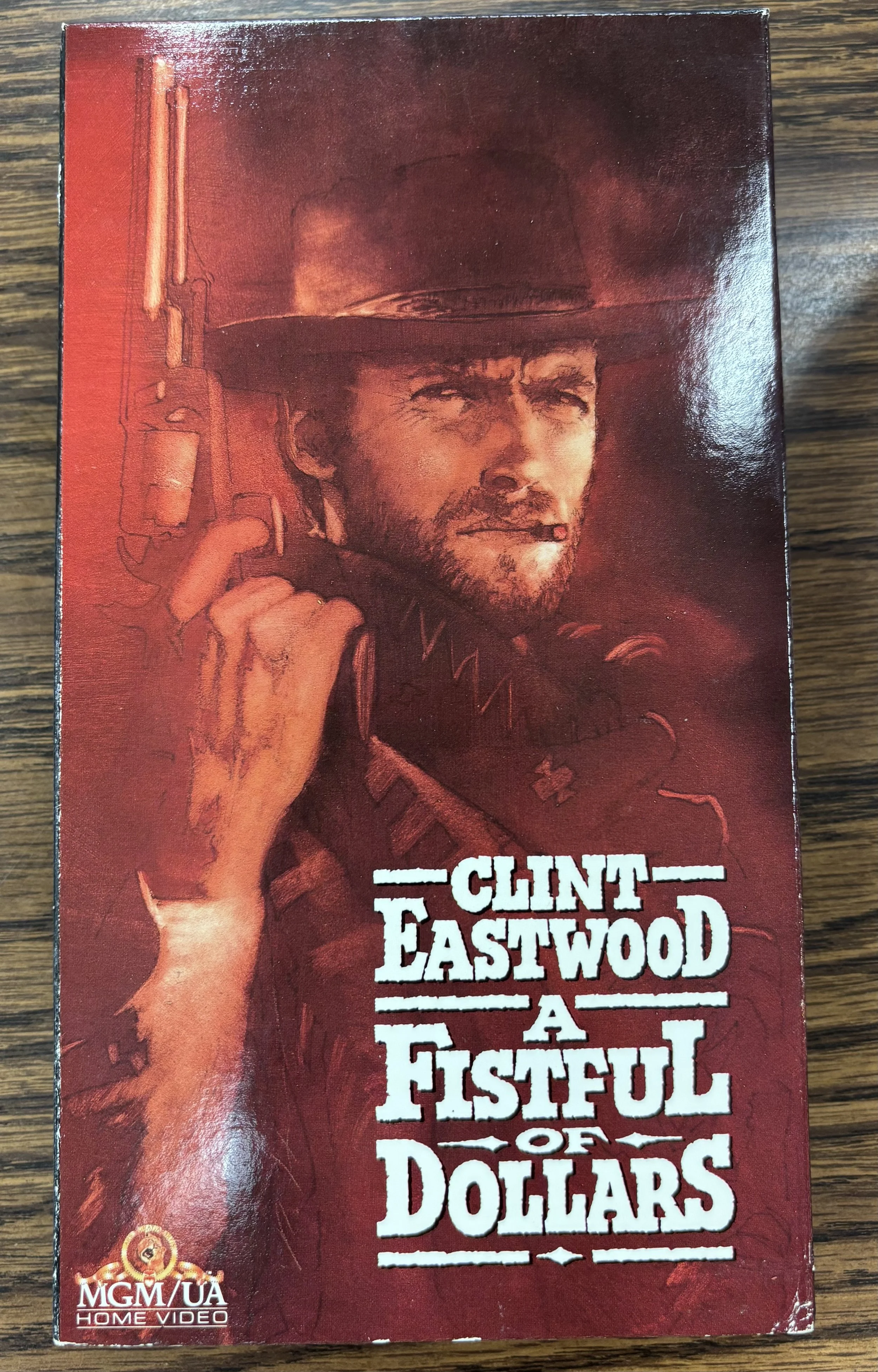 A rectangular VHS cover. It is all different shades of red. Clint Eastwood's character is displayed brandishing a pistol, wearing a cowboy hat and poncho. The film's title, Eastwood's name, and MGM/UA Home Video logo are printed on the bottom half.