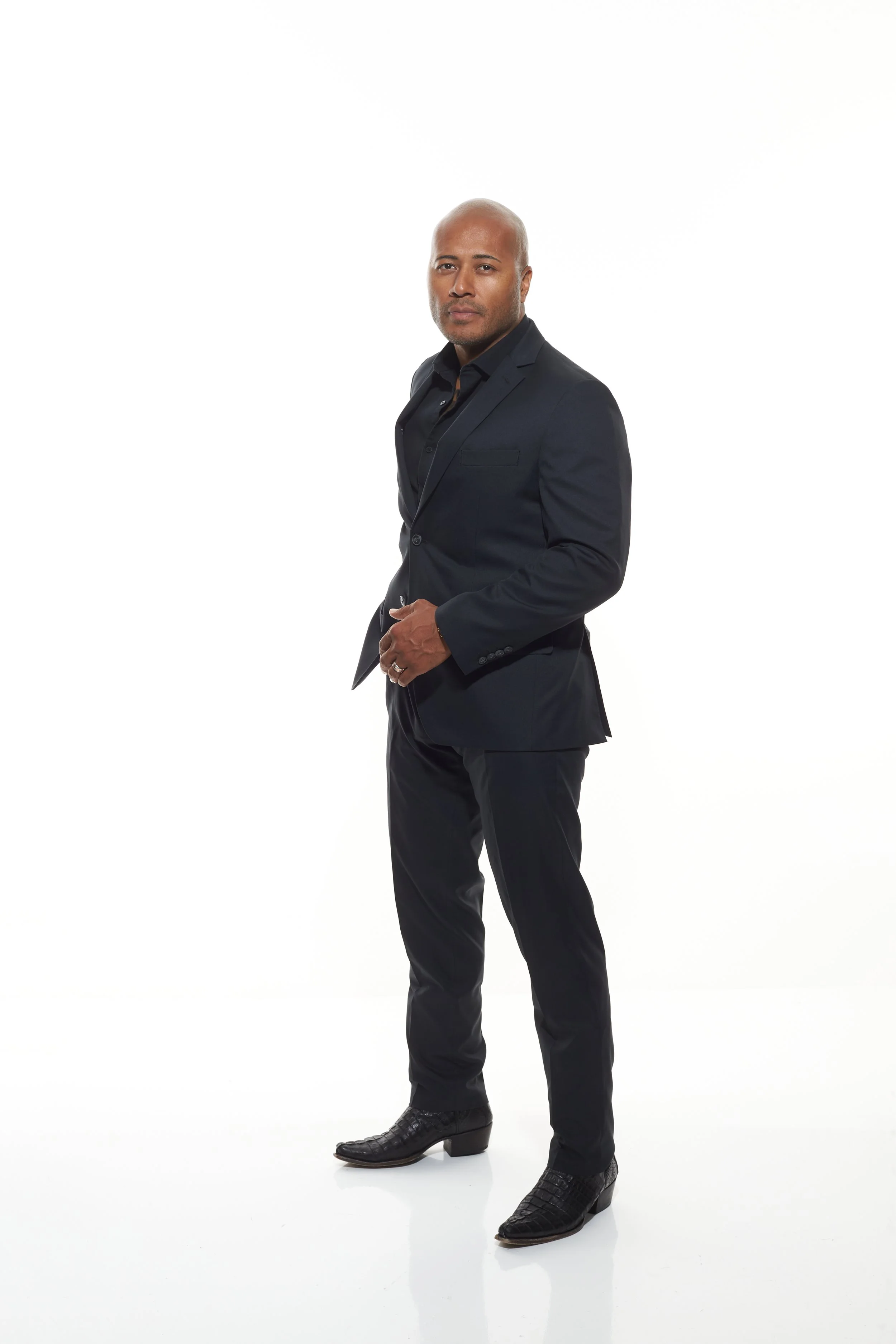 A man in a black suit standing against a white background
