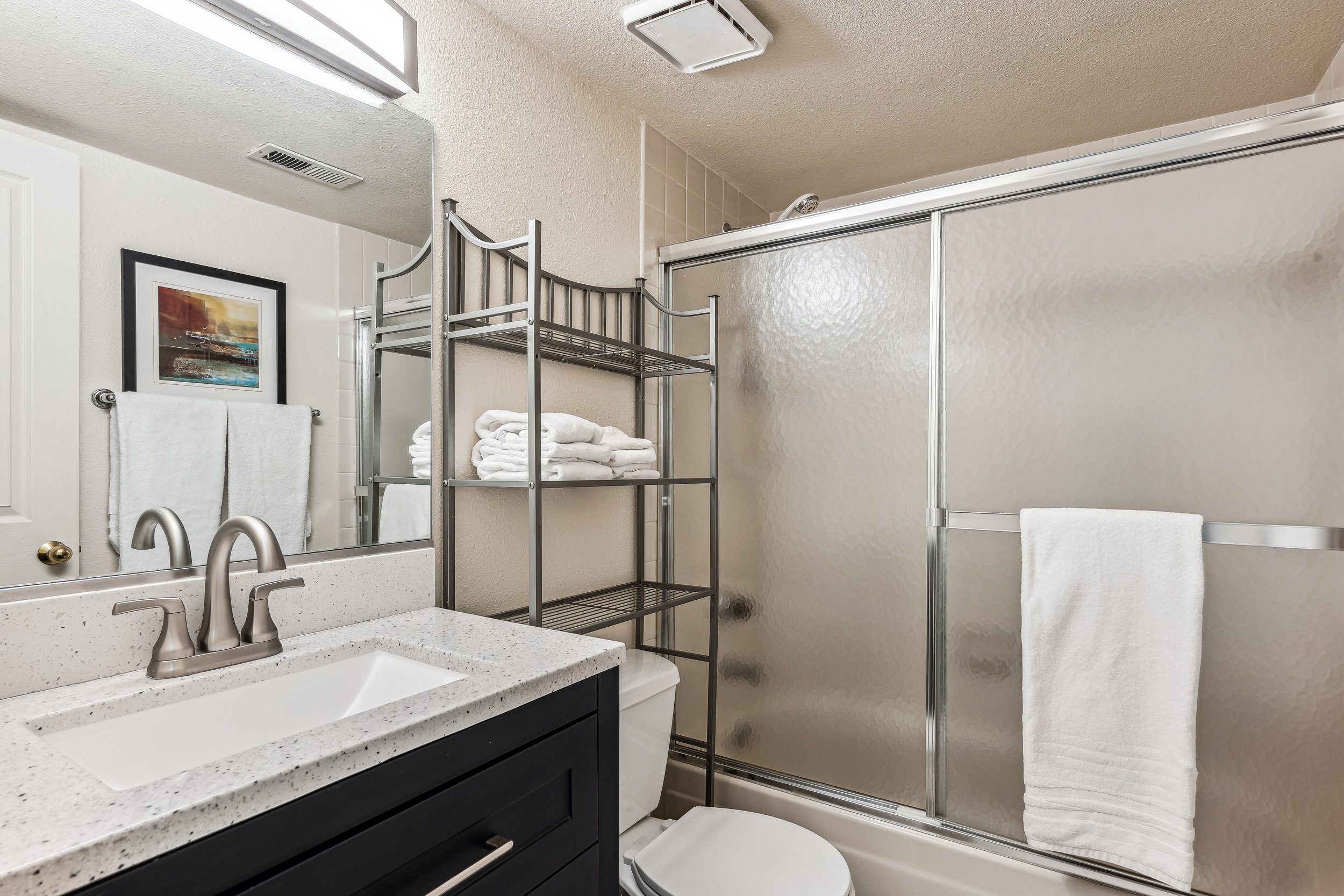 Unit 207 - A photograph of the smaller bathroom. Shower, toilet and sink featured.