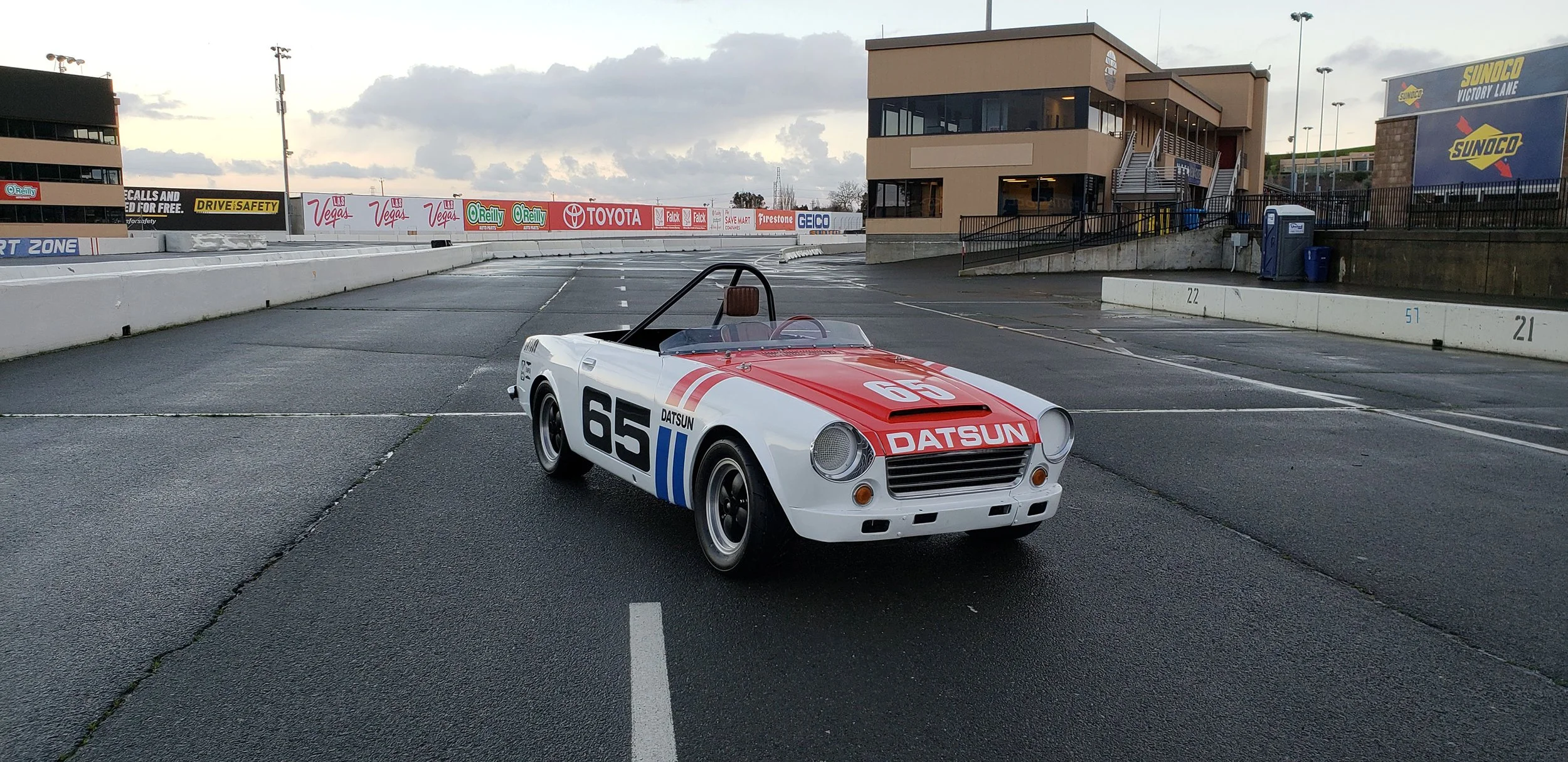 Front angle view photo of a vintage 1968 white race livery Datsun 1600 Roadster Fairlady car in a race track location. Bespoke build by premium car restoration and modification workshop Retro Sporting in California.