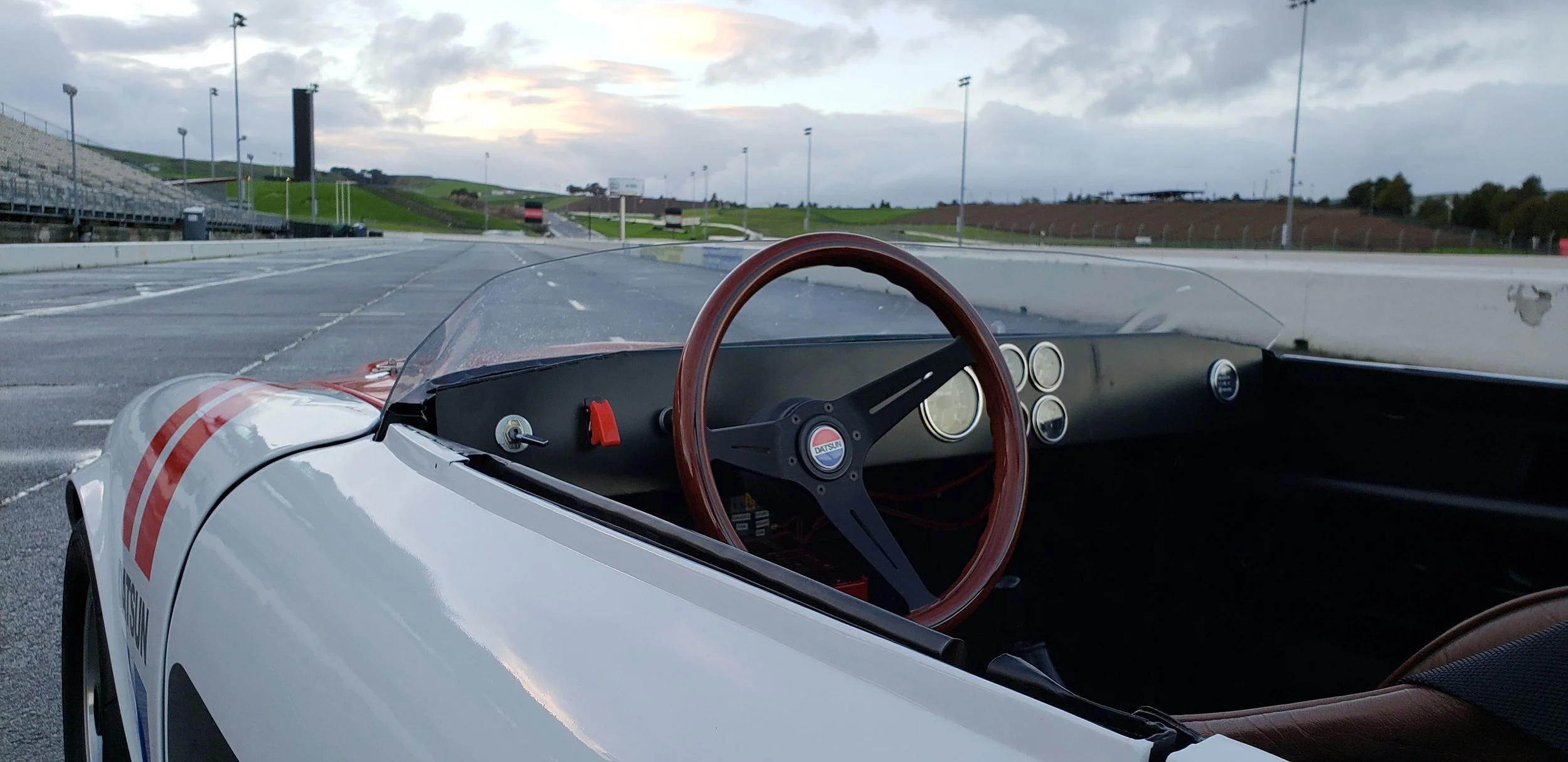 Interior cockpit detail photo of a vintage 1968 white race livery Datsun 1600 Roadster Fairlady car in a race track location. Bespoke build by premium car restoration and modification workshop Retro Sporting in California.