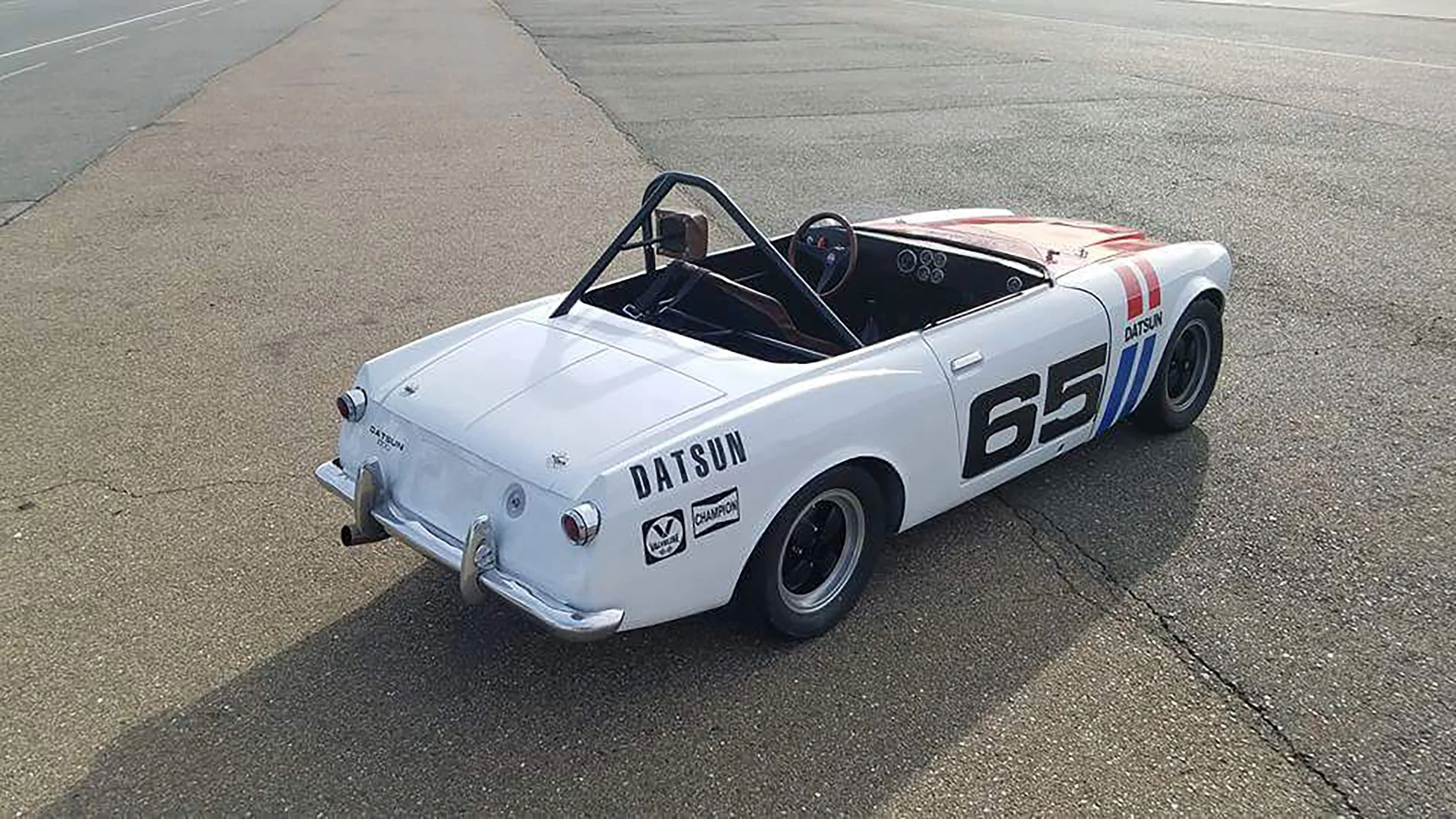 Top rear angle view photo of a vintage 1968 white race livery Datsun 1600 Roadster Fairlady car in a race track location. Bespoke build by premium car restoration and modification workshop Retro Sporting in California.