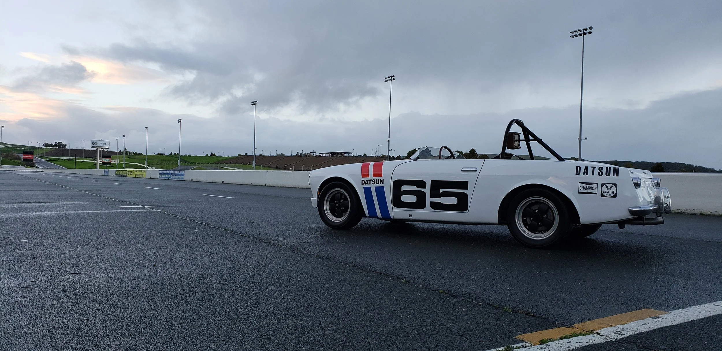 Side rear angle view photo of a vintage 1968 white race livery Datsun 1600 Roadster Fairlady car in a race track location. Bespoke build by premium car restoration and modification workshop Retro Sporting in California.