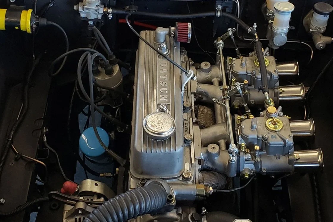 Engine detail photo of a vintage 1968 white race livery Datsun 1600 Roadster Fairlady car in a race track location. Bespoke build by premium car restoration and modification workshop Retro Sporting in California.