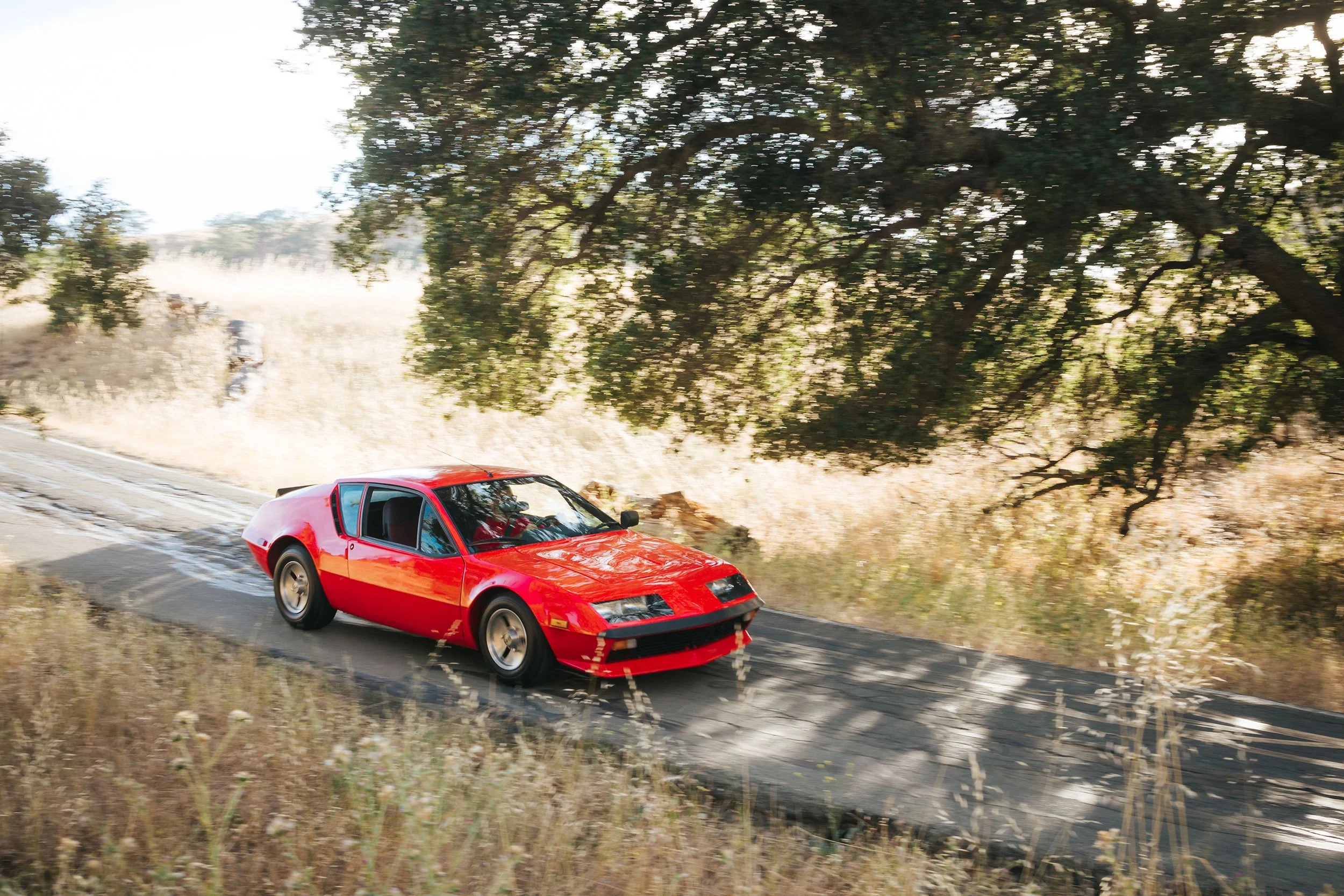 Front angle view photo of a vintage 1980 red Alpine A310 car in a country road location. Bespoke build by premium car restoration and modification workshop Retro Sporting in California.