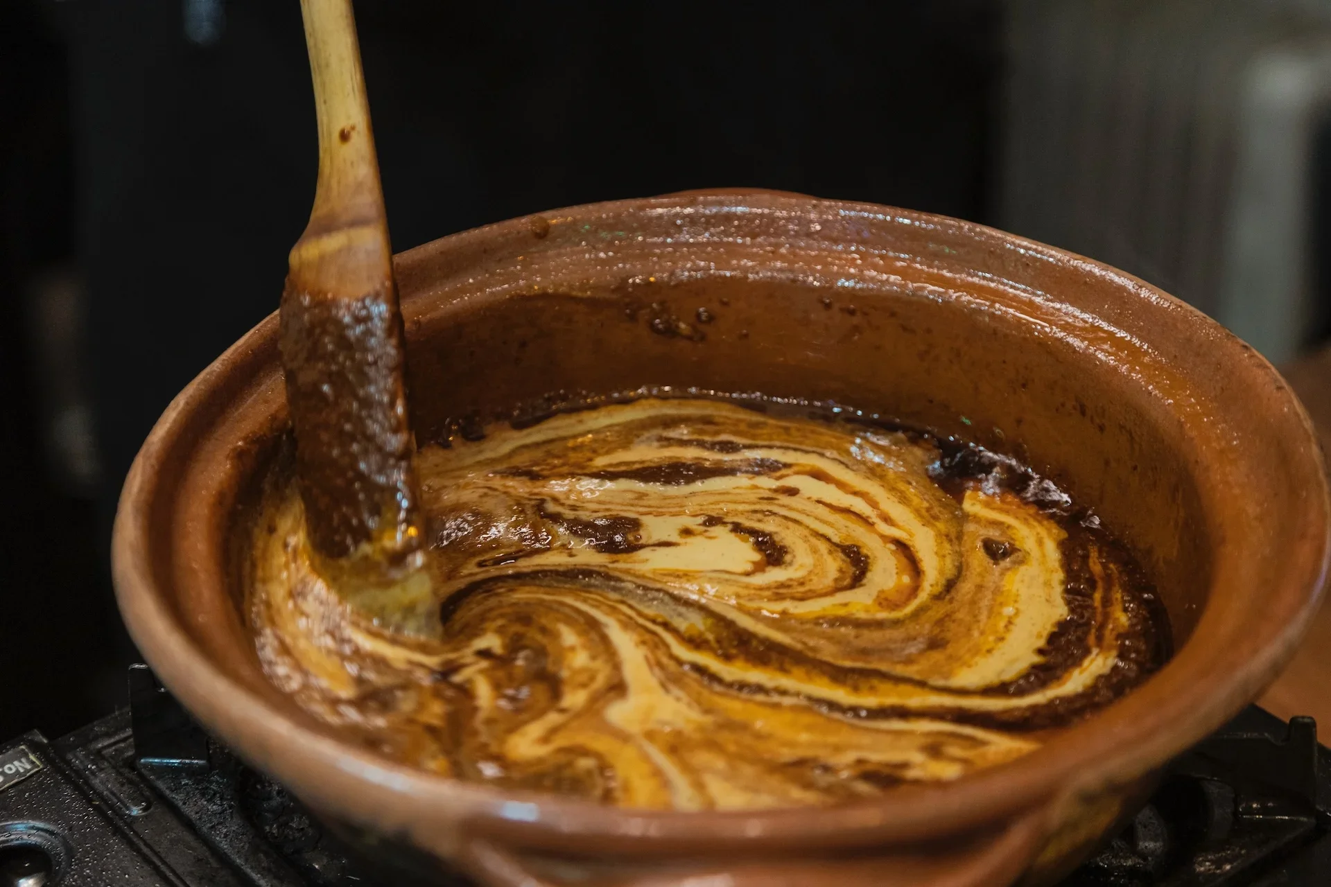 Ceramic mug contains hot chocolate with swirled whipped cream and chocolate sauce, with a cinnamon stick resting against the rim.
