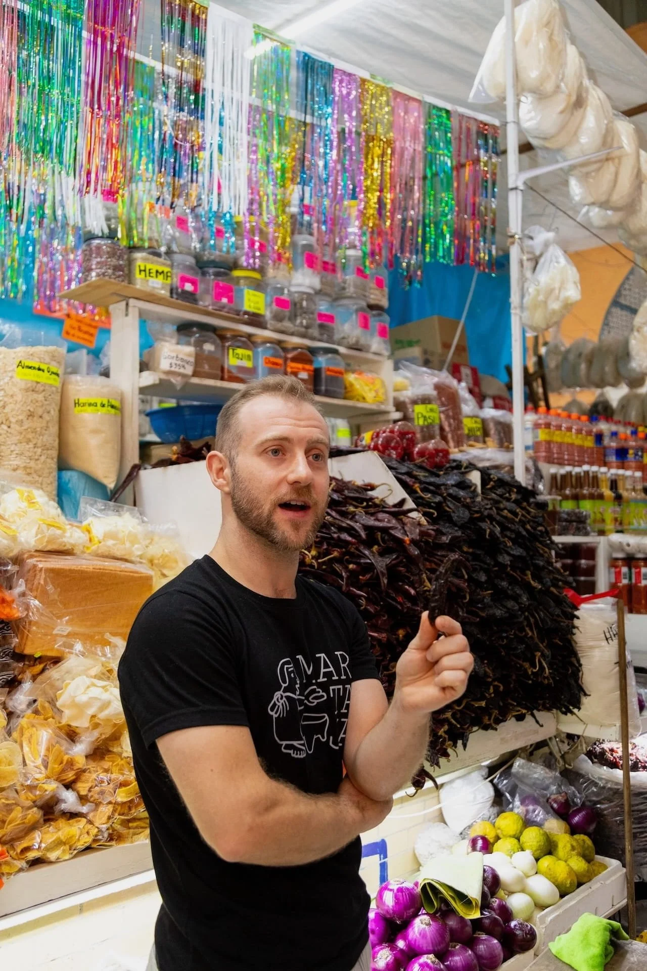 A Martaja chef stands in front of a colorful spice stall at Colonia Roma's Medellín Market, explaining the history of contemporary Mexican cuisine