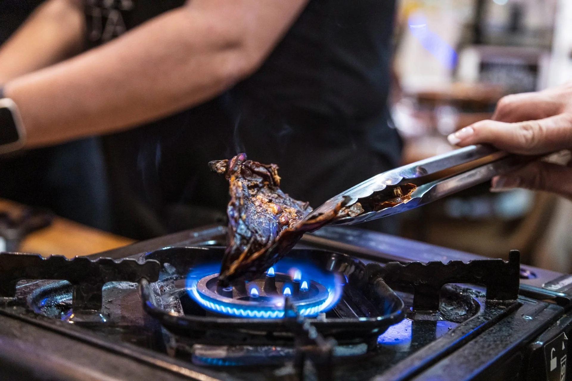 A guest toasts dried ancho chile peppers on a blue gas flame in order to char them for making mole.