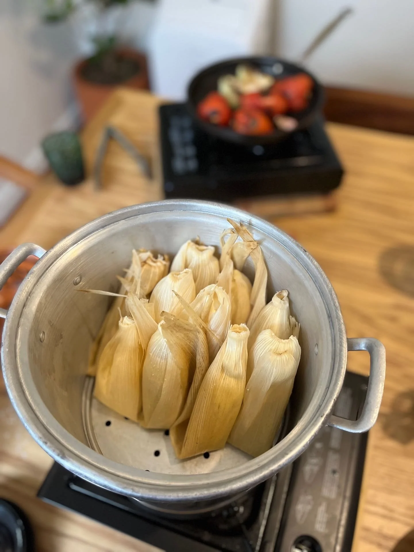 Tamales wrapped in corn husks sit in a steamer with tomatoes and other ingredients for smoky chipotle salsa being charred in the background in a beautiful Condesa apartment that hosts cooking classes.