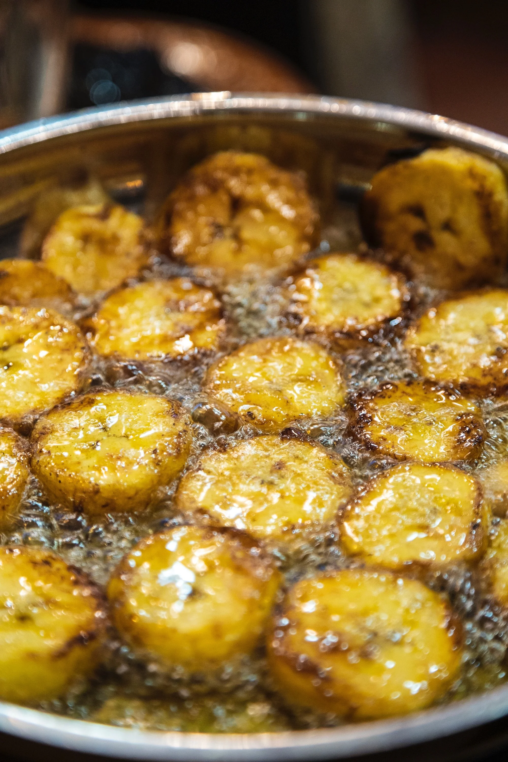 Fried plantains frying in hot oil in a stainless steel pan.