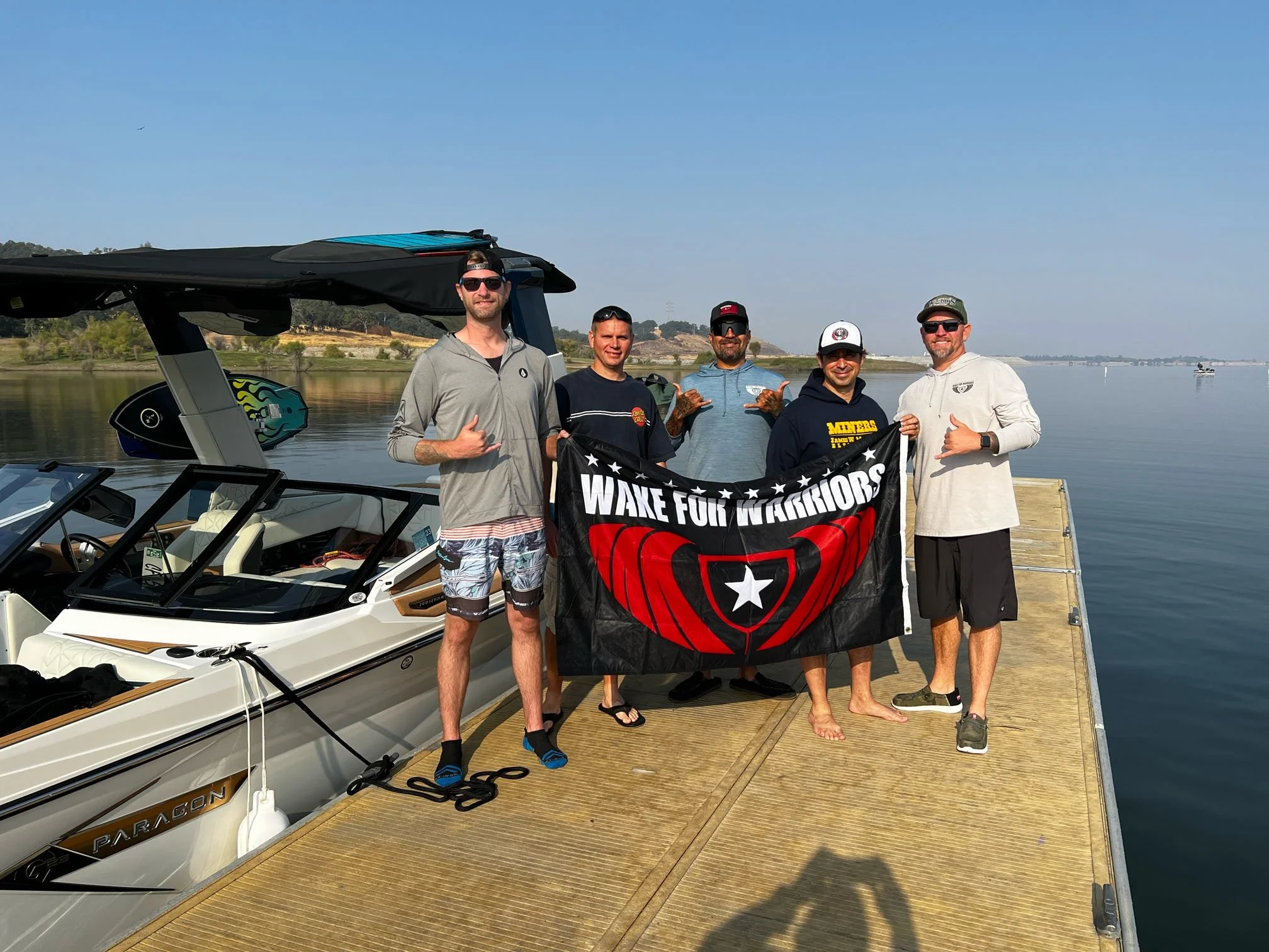 Veterans stand next to a boat and hold a Wake for Warriors flag