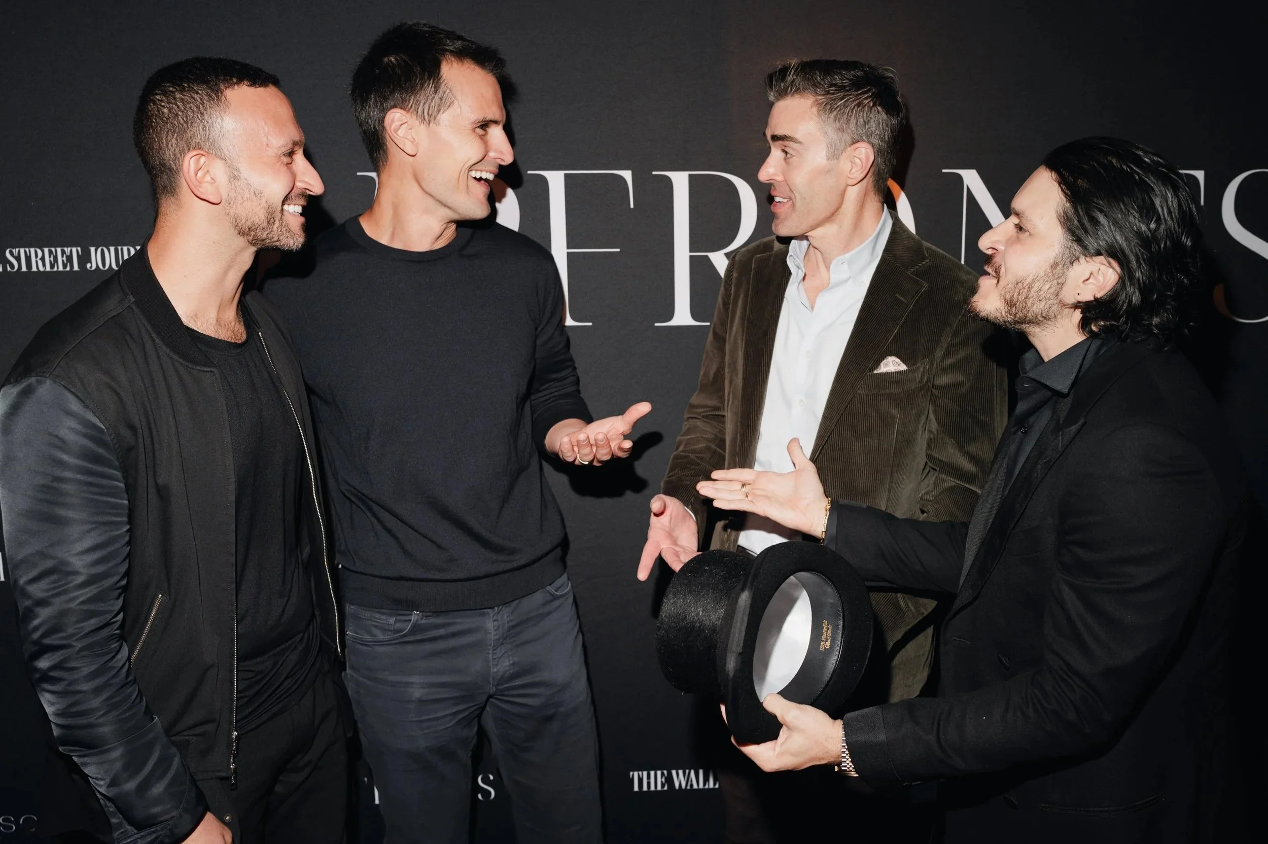 A group of people socializing at an indoor event, wearing formal attire, and holding drinks in a lively atmosphere.