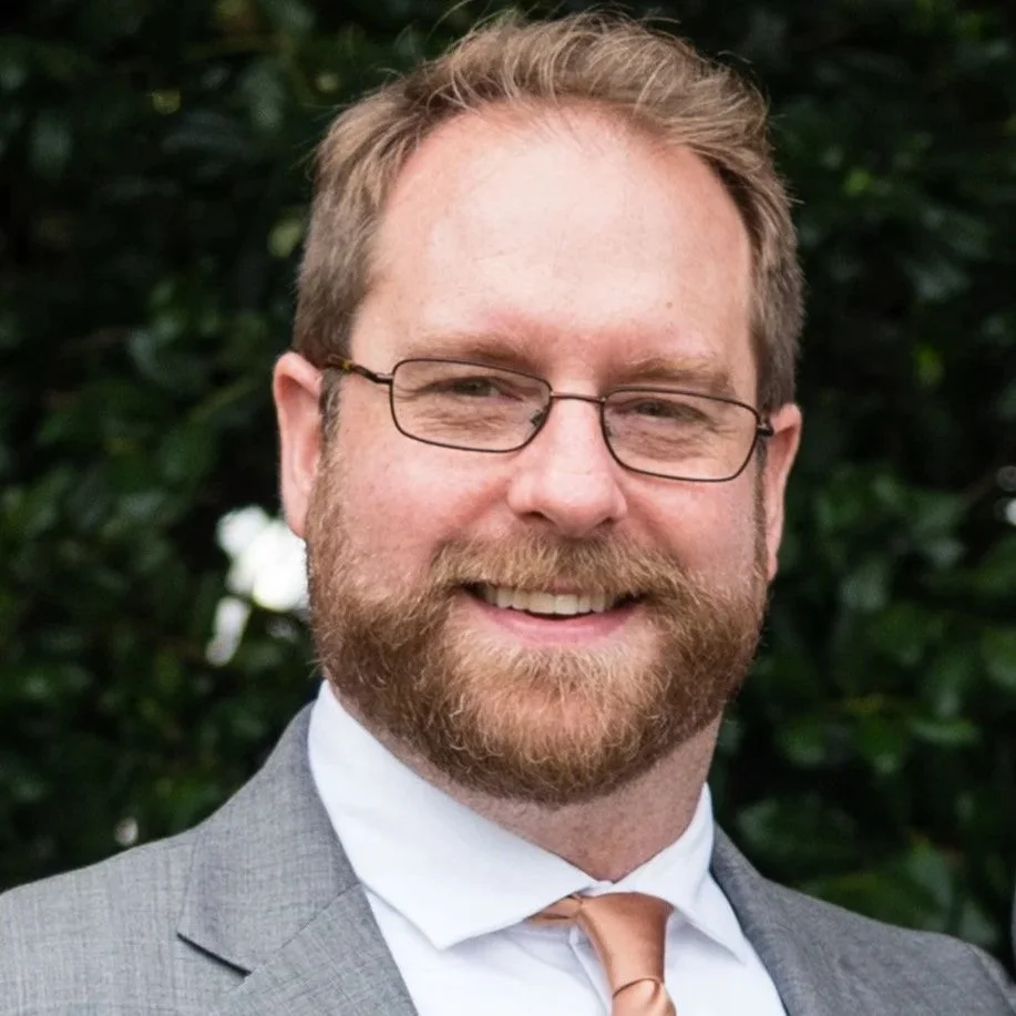 Dr. David Baker wearing a gray suit, white shirt, and a light-colored tie.