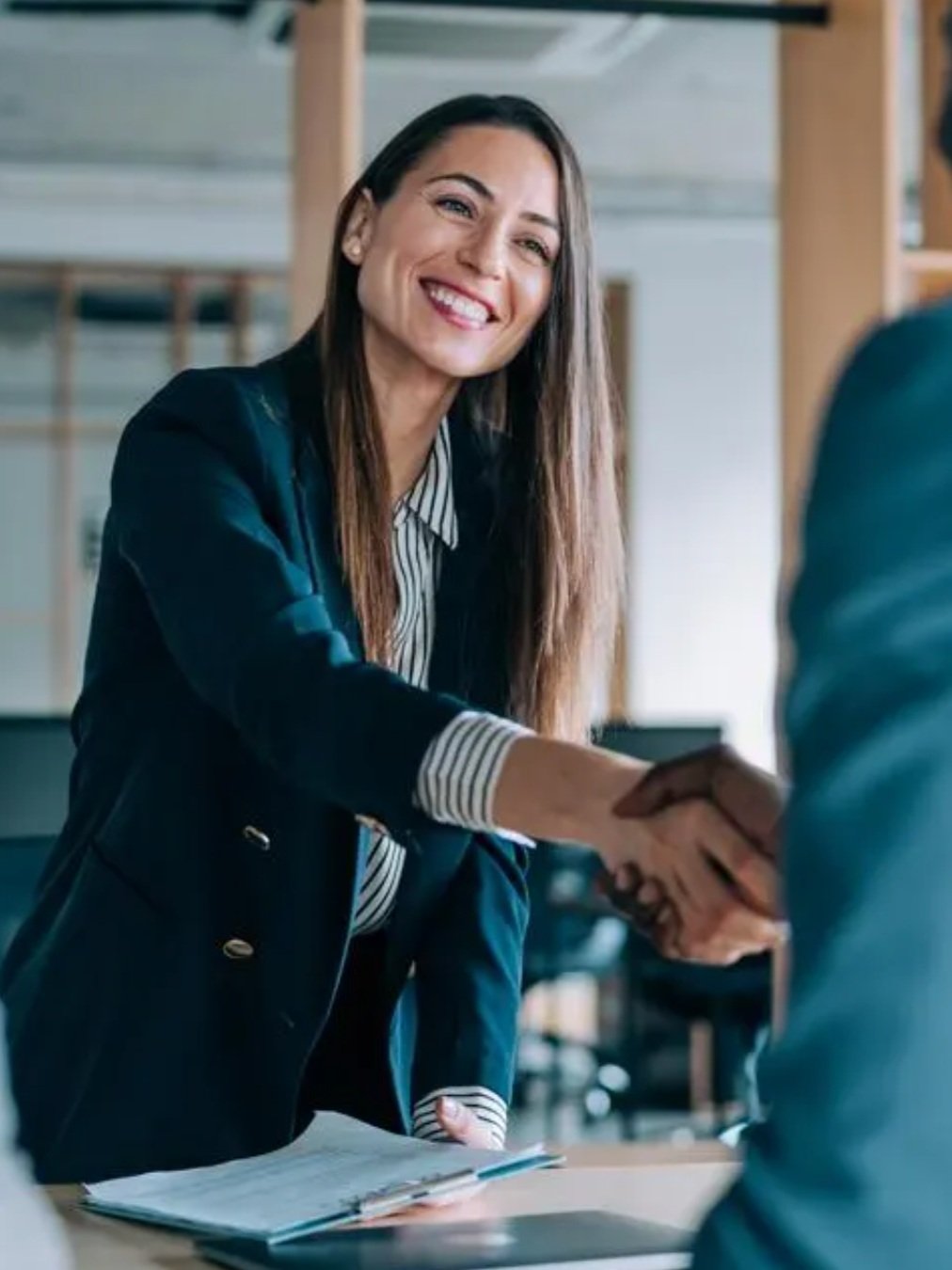 A woman smiles and shakes someone's hand, who is out of frame. She is networking.