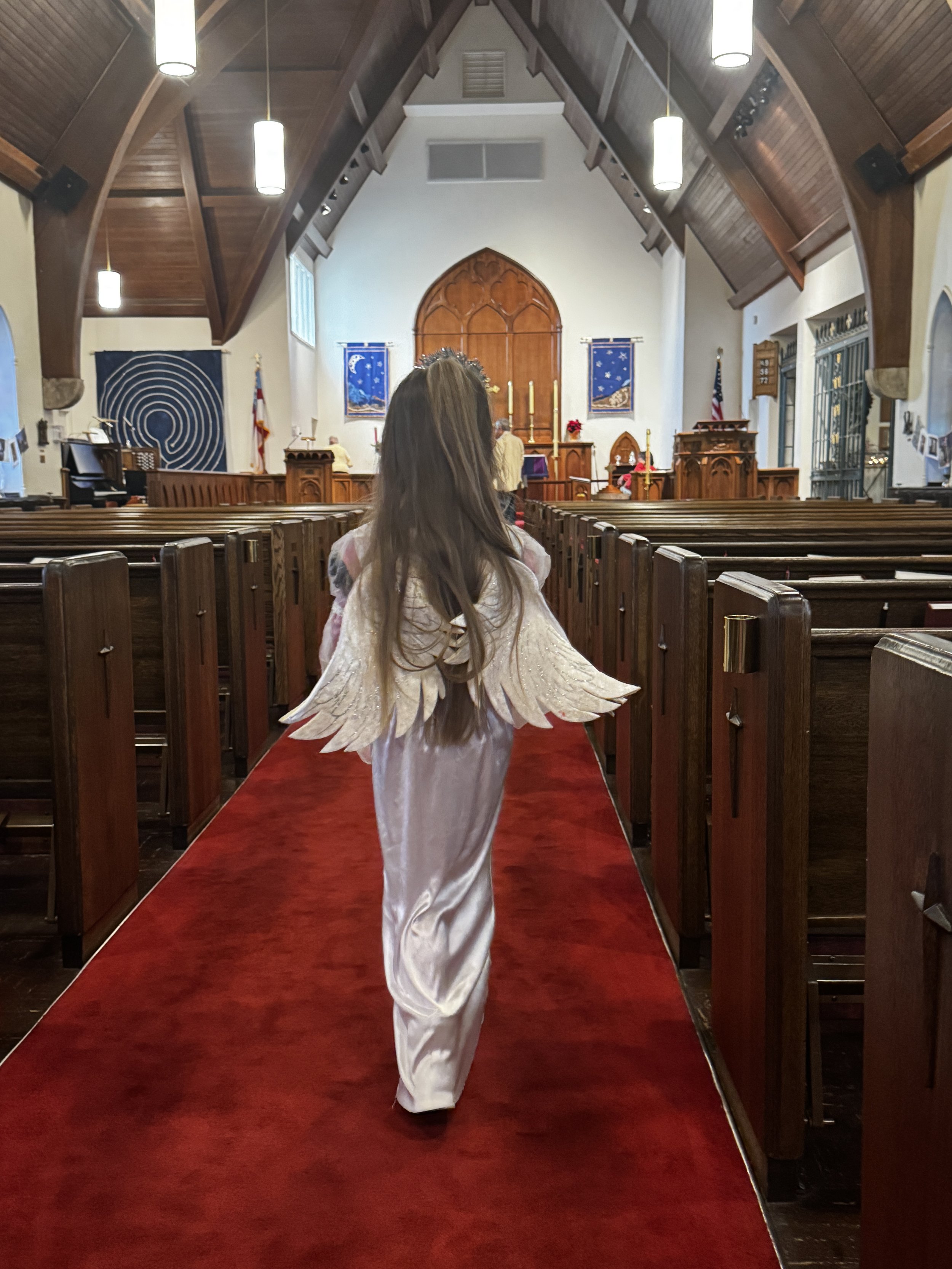 girl in angel costume walks down the church aisle