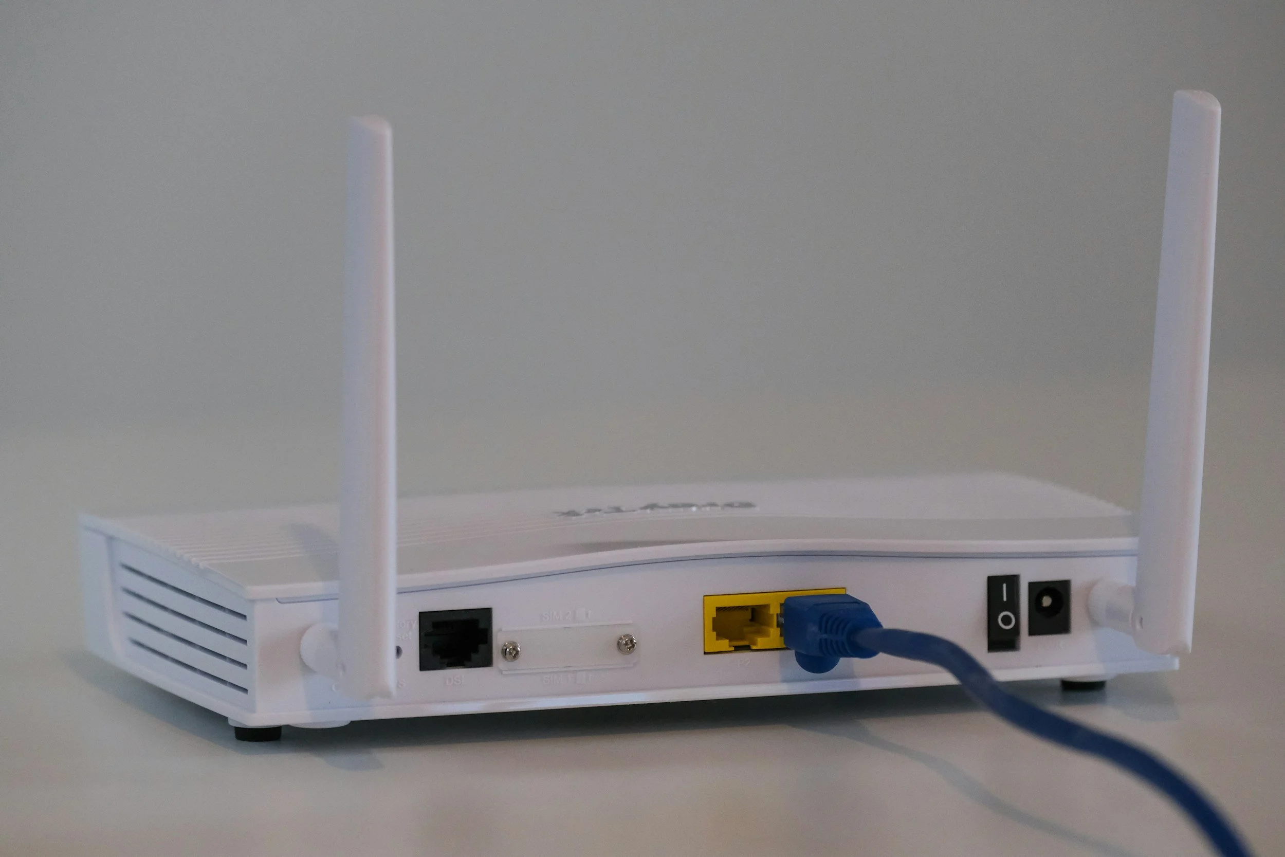 A white Wi-Fi router with two antennas connected to a modem via an Ethernet cable.