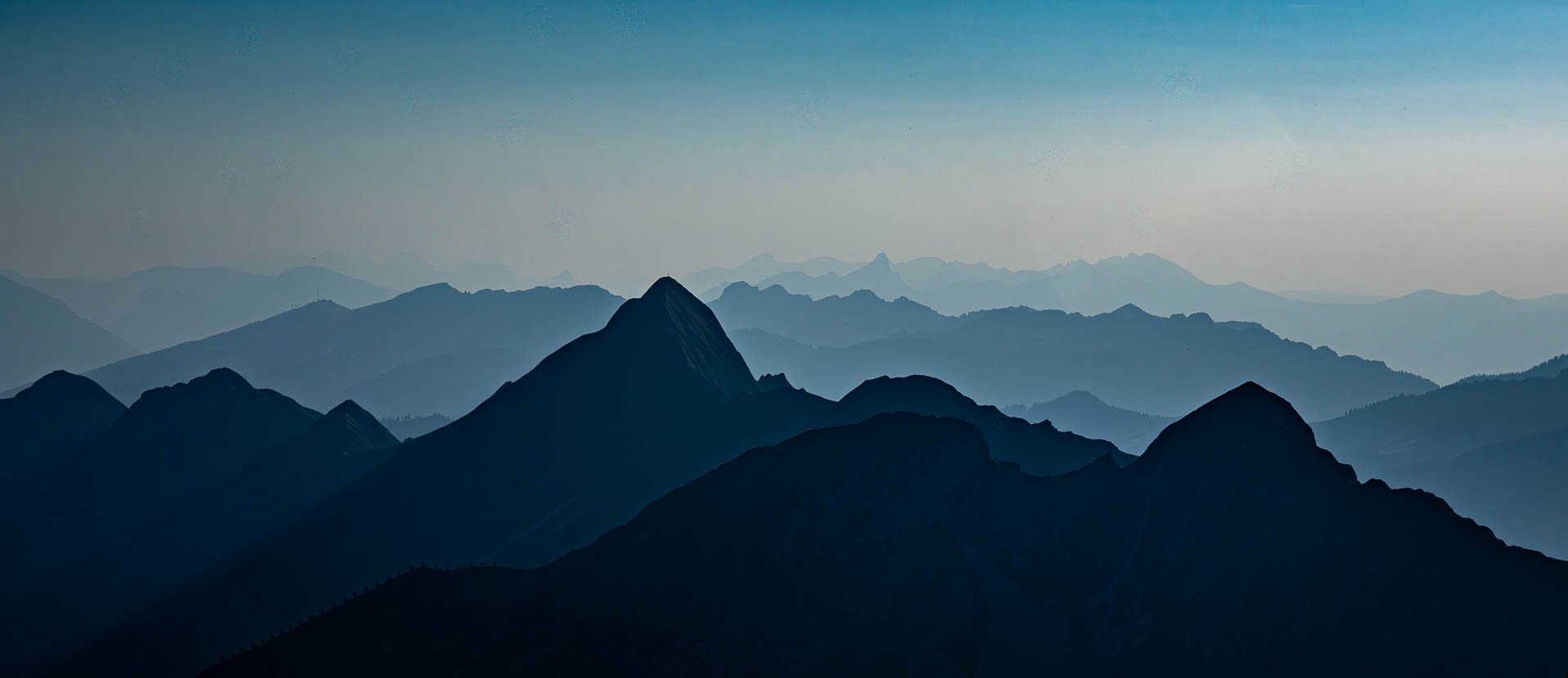 Bergkette mit mehreren Gipfeln in verschiedenen Blautönen unter einem klaren Himmel.
