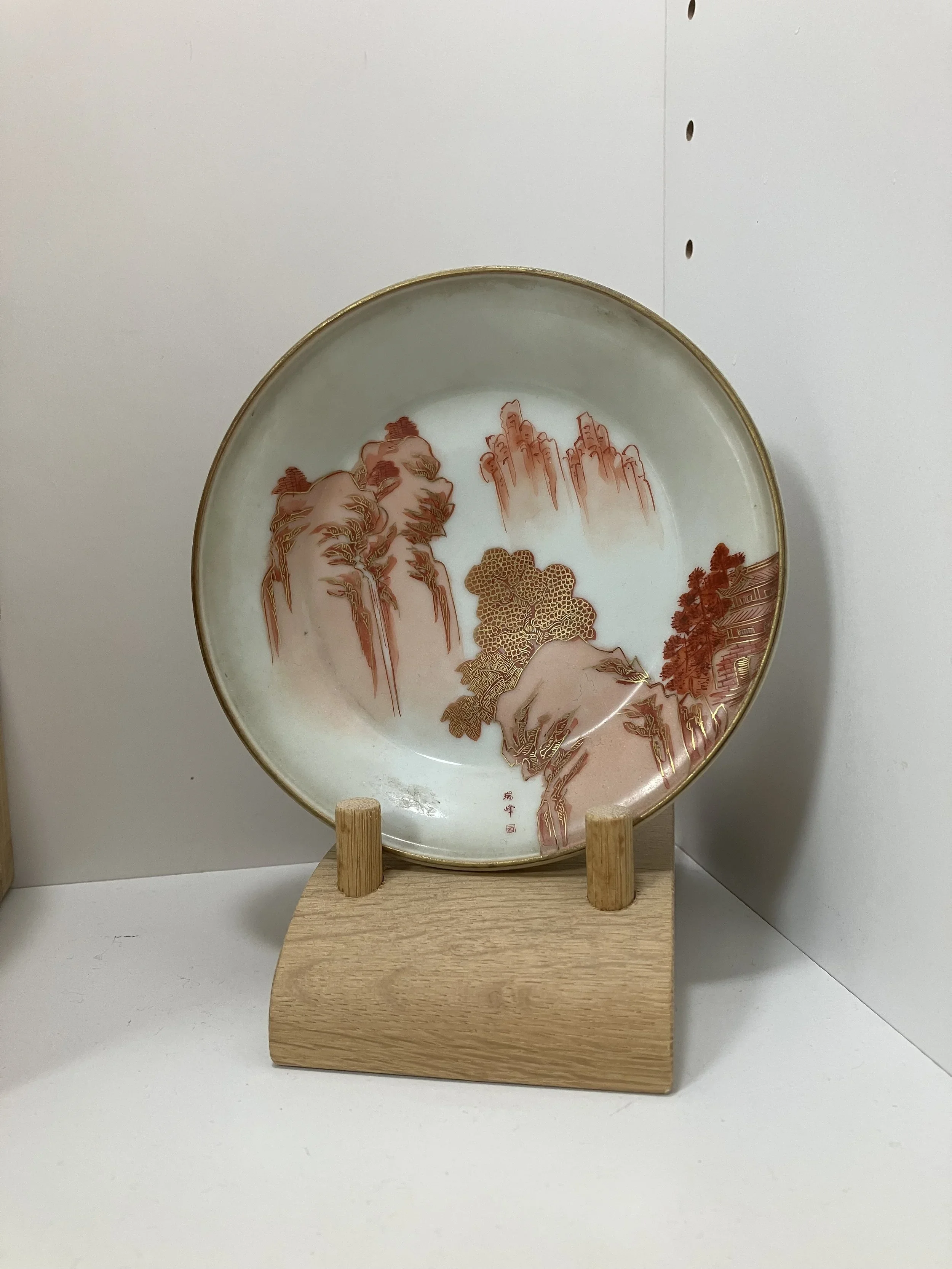Chinese porcelain plate with mountain landscape design, displayed on a wooden stand.