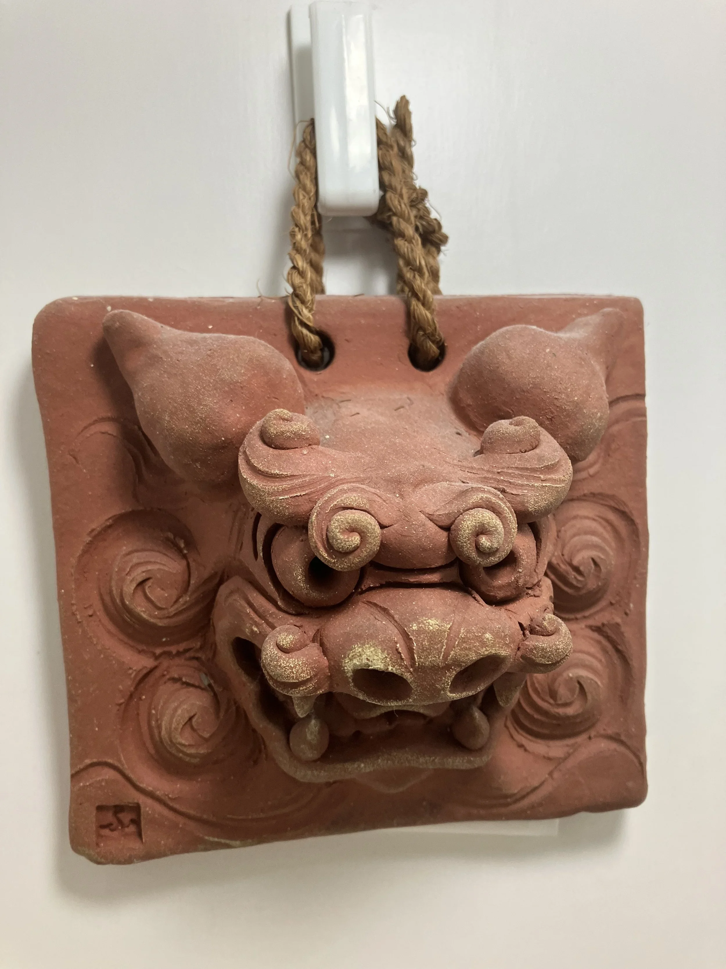 Terracotta Chinese dragon door ornament hanging on a white wall.