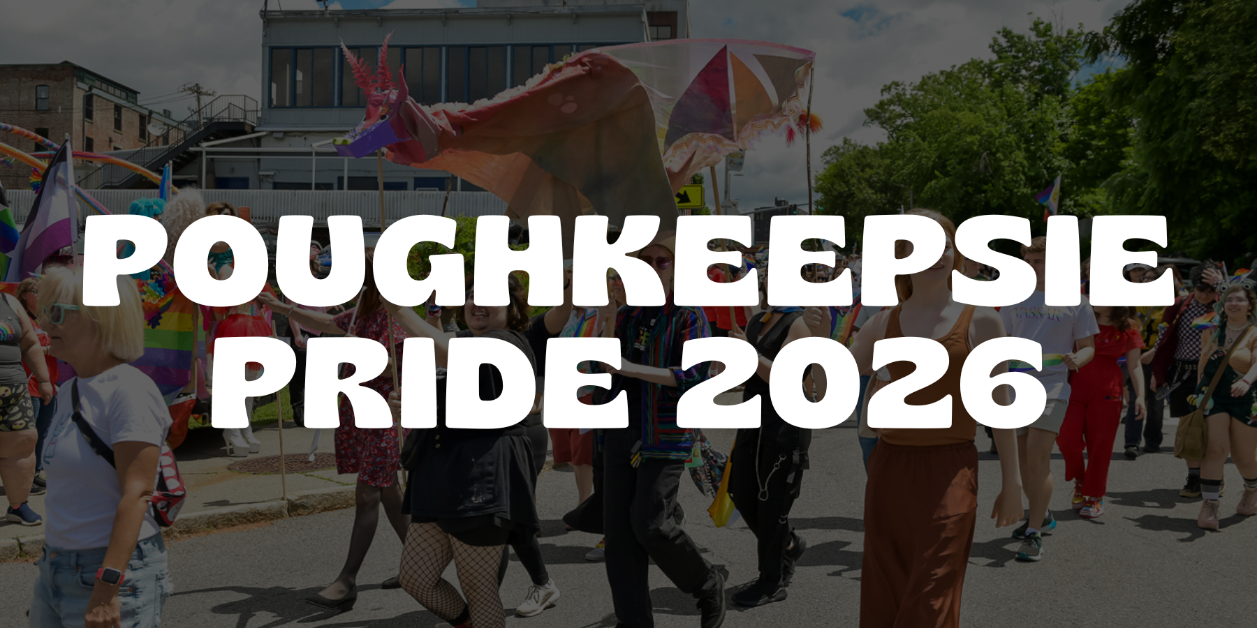 People participating in the Poughkeepsie Pride 2026 parade, some holding rainbow flags and a large unicorn-themed float, during daytime with a cloudy sky.