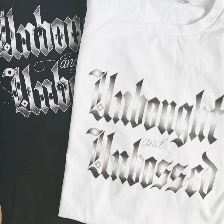 white t-shirt on top of a black t-shirt with the words Unbought and Unbossed written in blackletter in vinyl