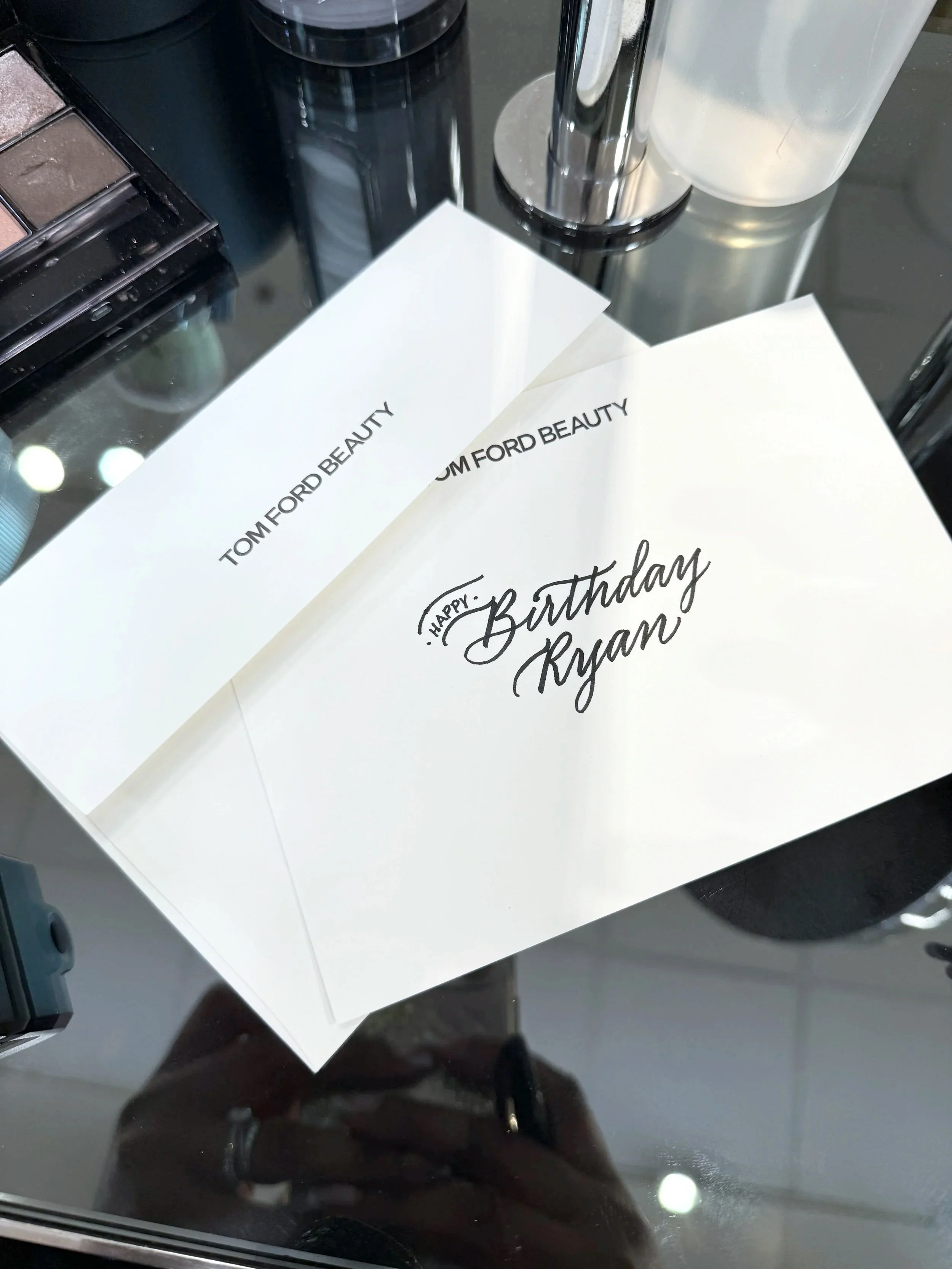 white envelope with black calligraphed words for a birthday sentiment atop a cosmetics table at a Tom Ford activation