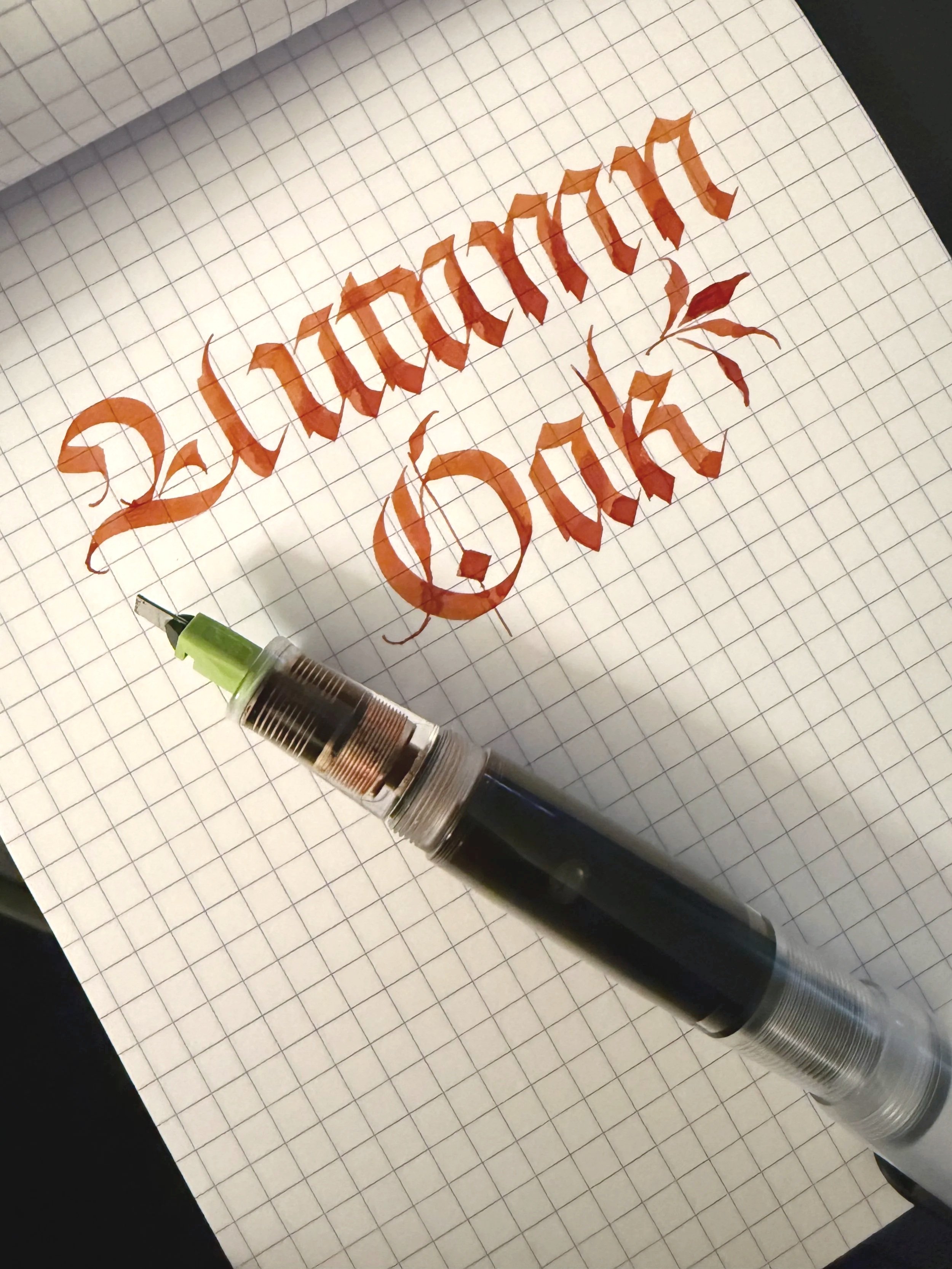 The words Autumn Oak in brown ink on a grid notebook sheet with a converted pilot parallel pen