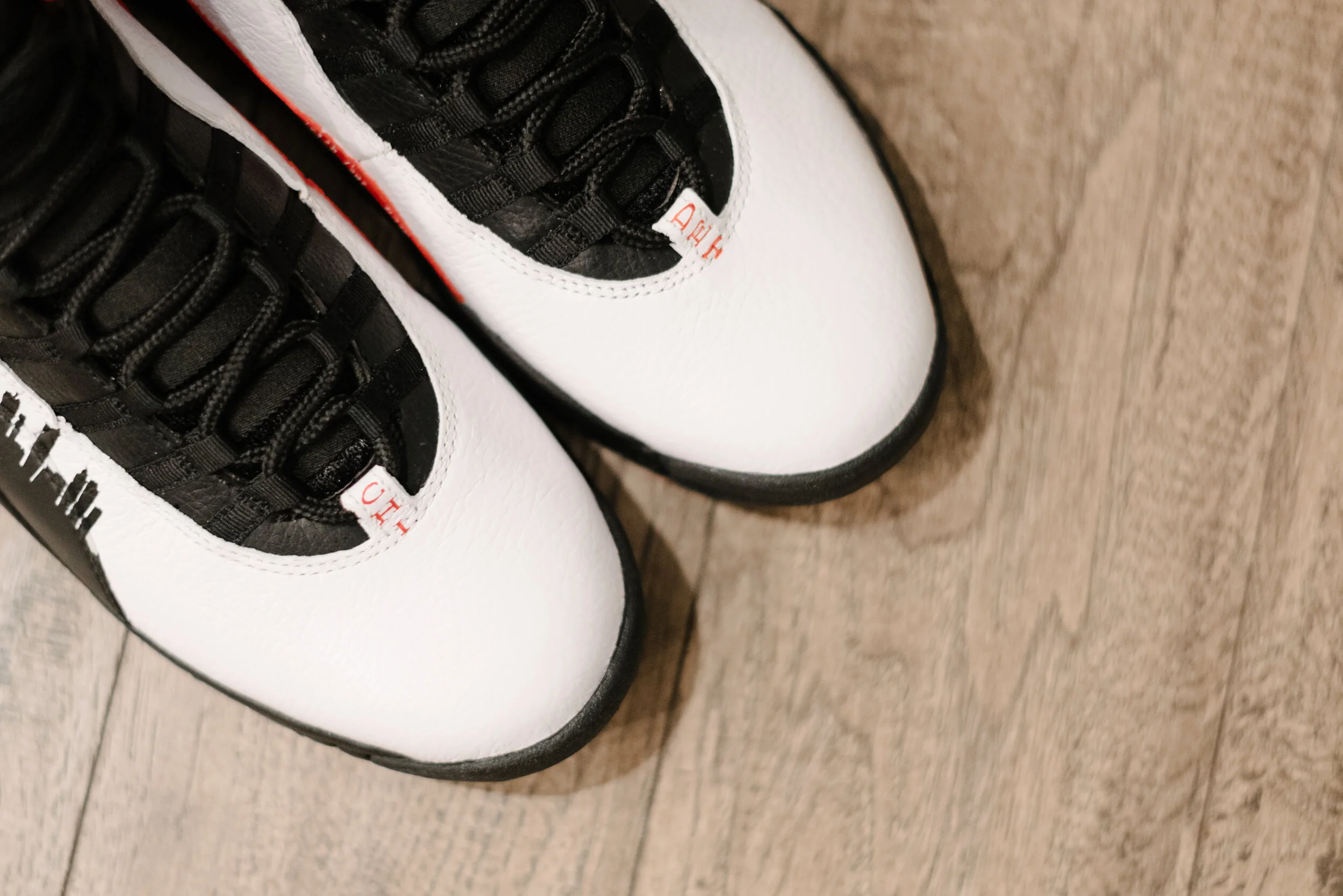 Close-up of white sneakers with black laces on a wooden floor.