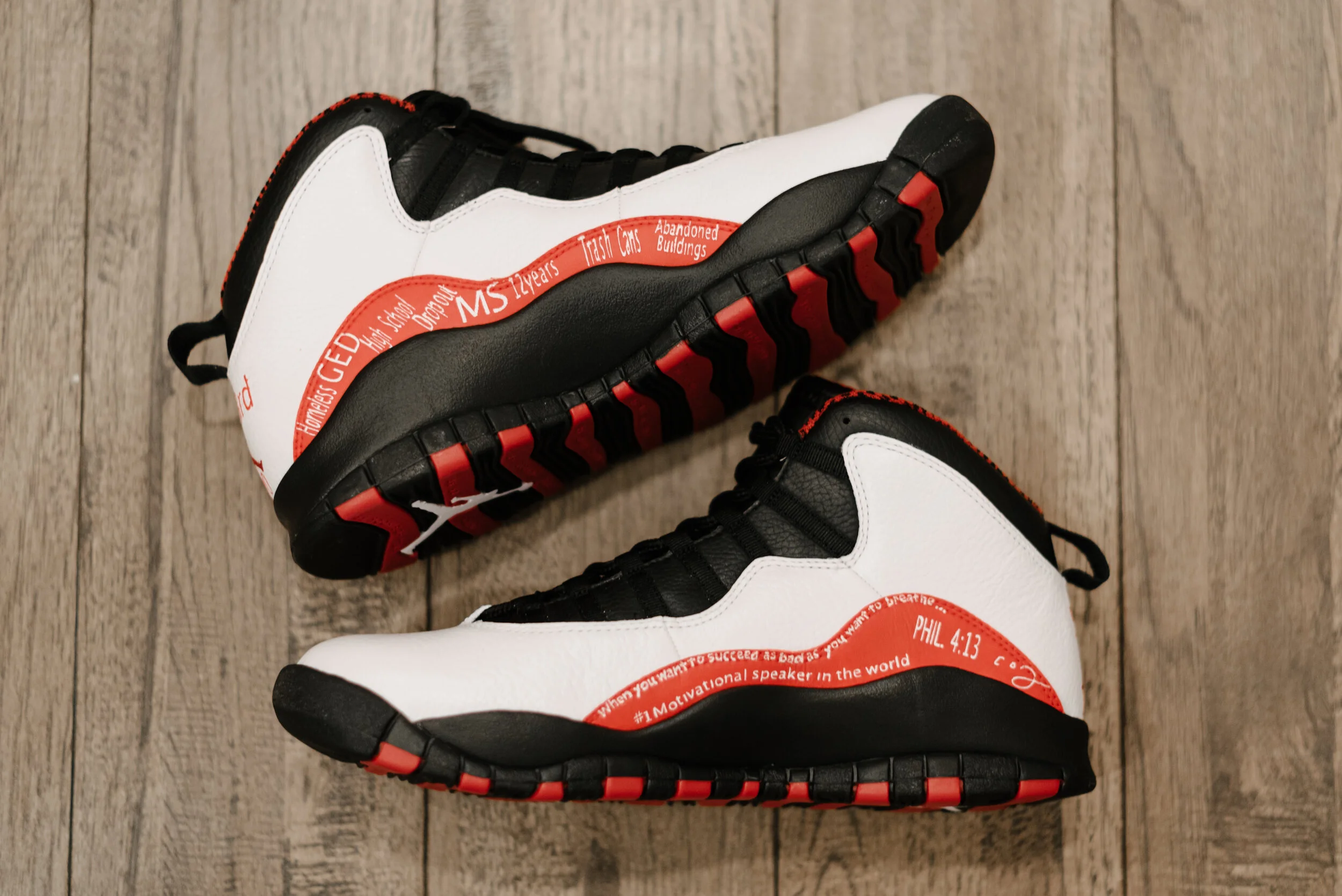 Pair of Nike Air Max sneakers with black, white, and red accents on a wooden floor.